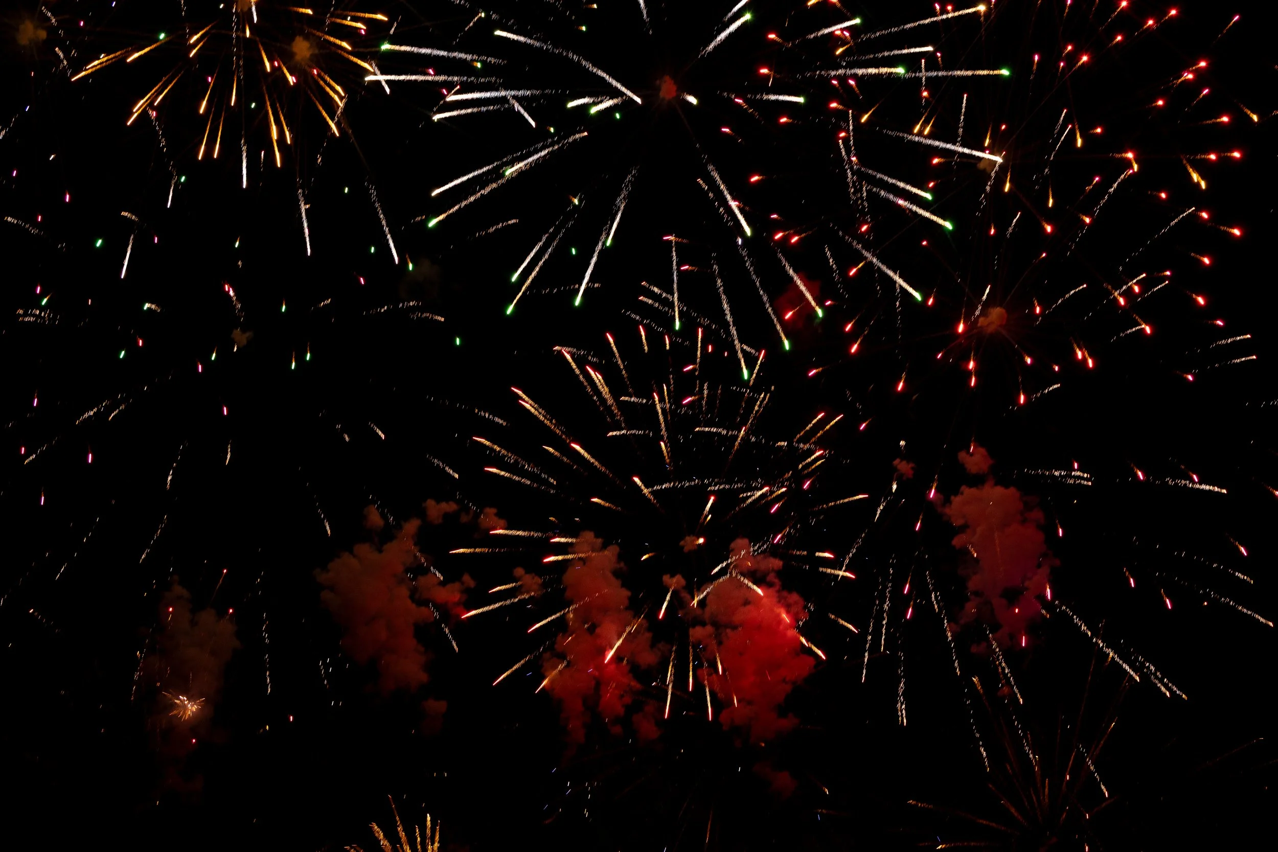 Colorful fireworks exploding in the night sky with streaks of red, green, and white light, and some smoke clouds.