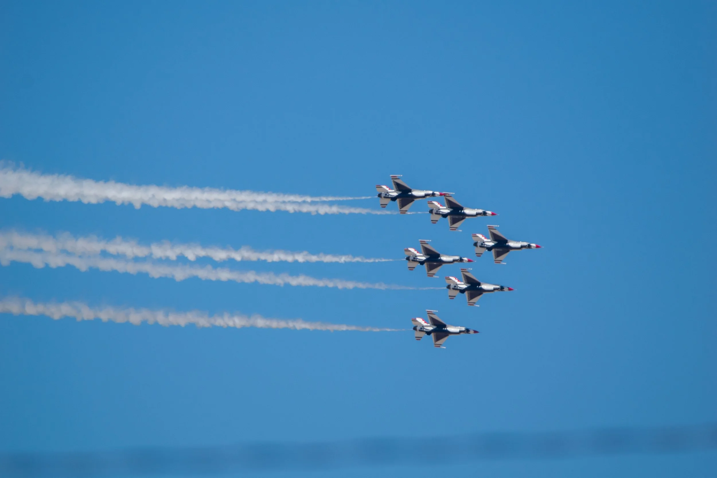 Six fighter jets flying in formation with white smoke trails against a clear blue sky.