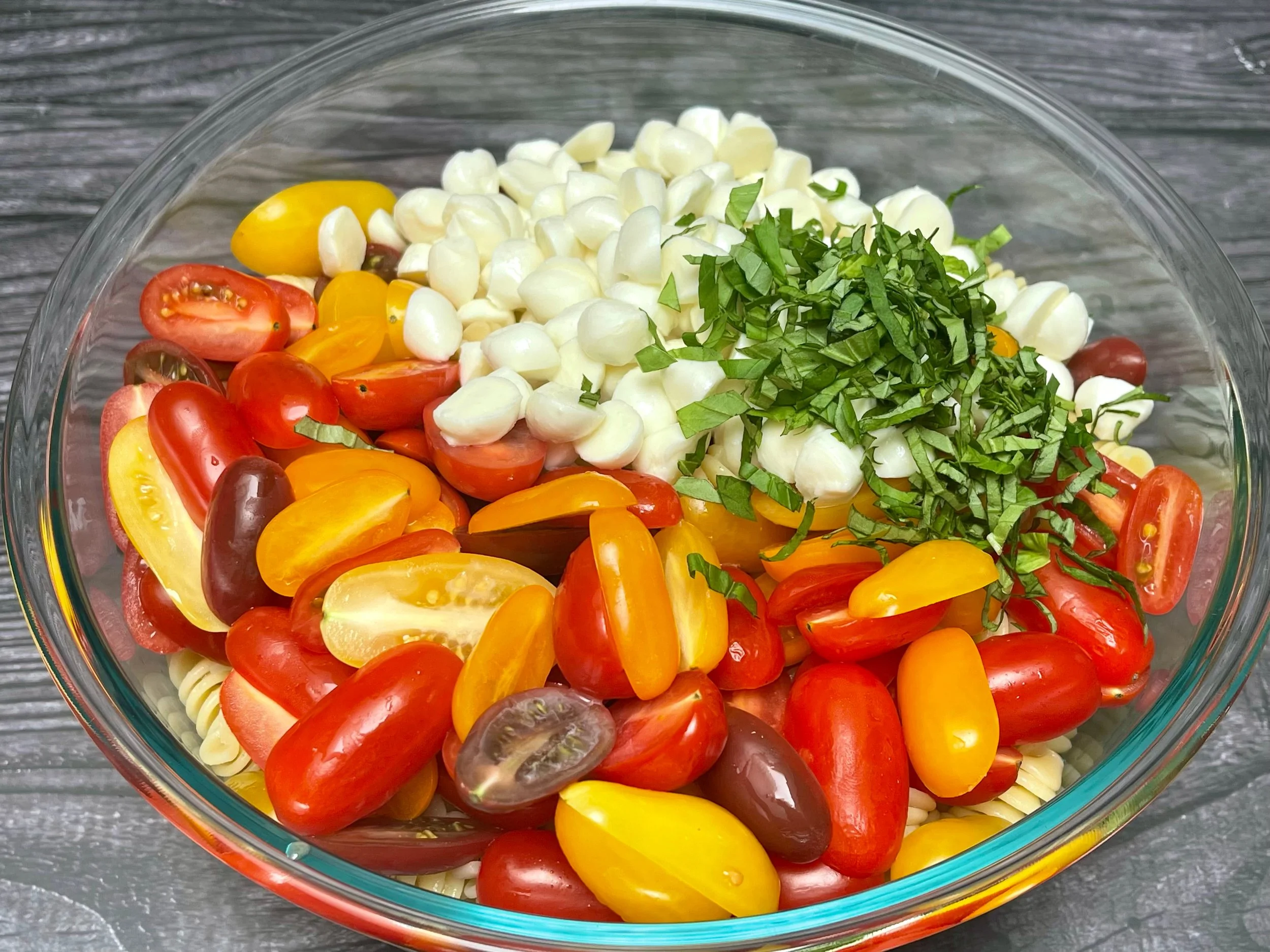 Mixing in tomatoes, mozzarella, and basil