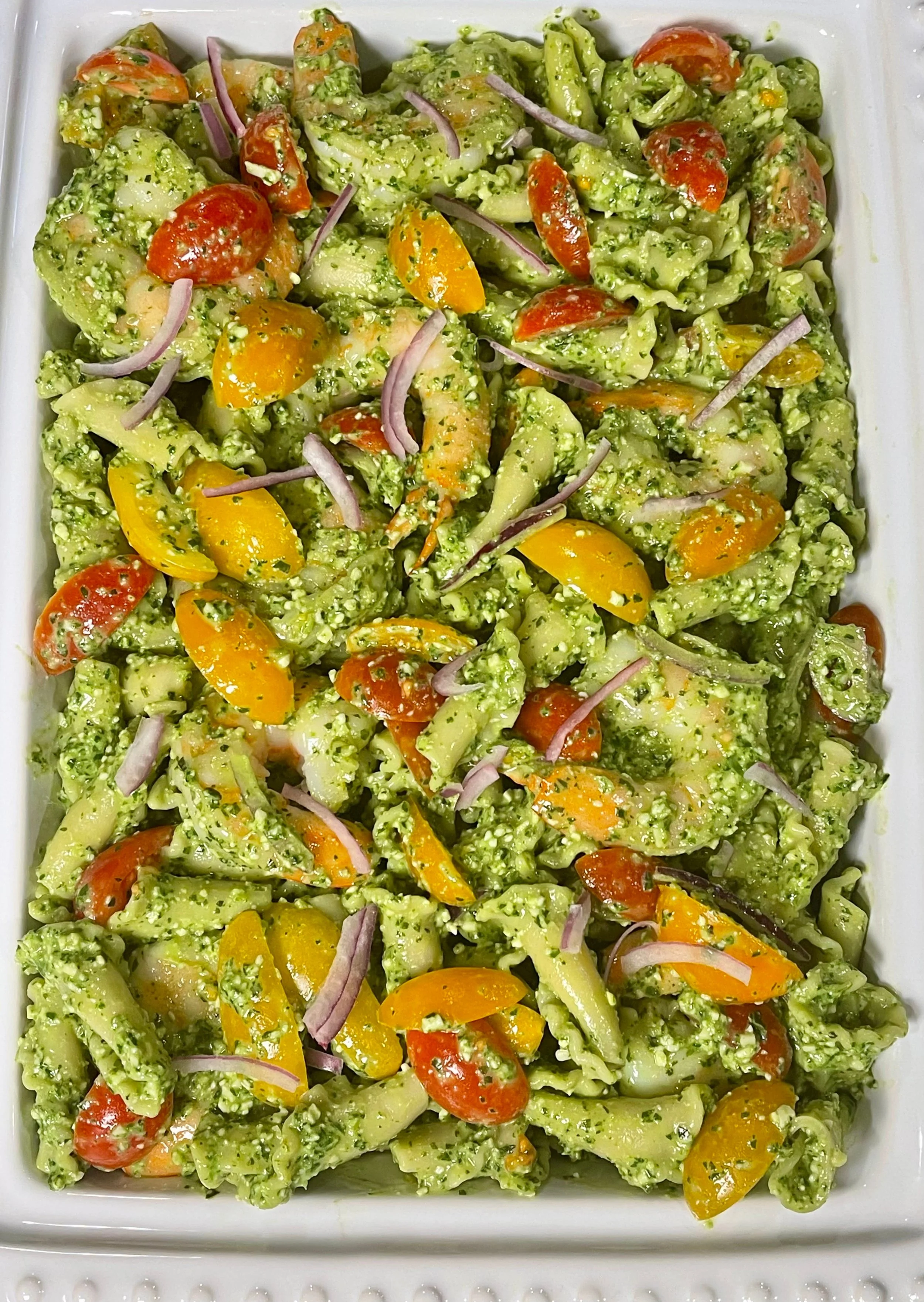 Shrimp pesto pasta salad in serving dish topped with remaining red onions