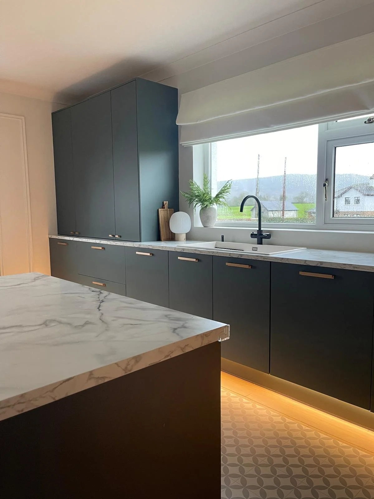 Kitchen detail with deep-toned cabinetry, marble-effect worktops, and warm under-cabinet lighting.