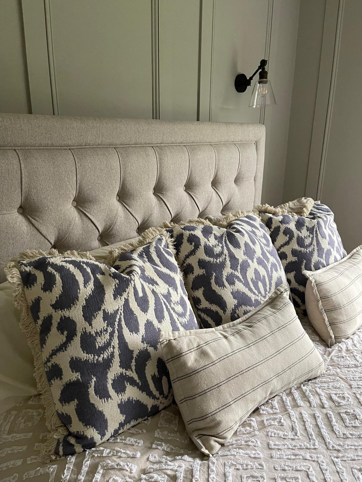 Close-up of the bed styling with a tufted headboard, patterned cushions, and softly layered textiles.