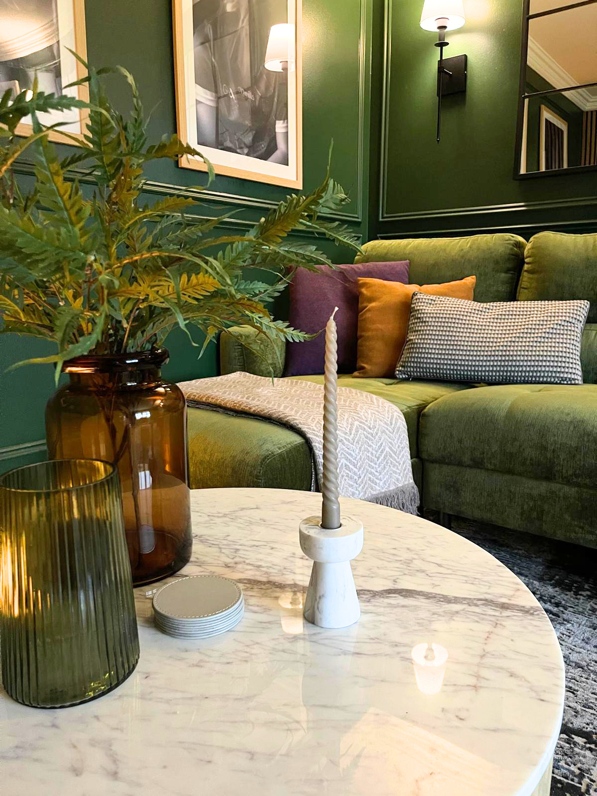 Styling detail with marble-effect coffee table, greenery, and warm metallic accents against the deep green backdrop.