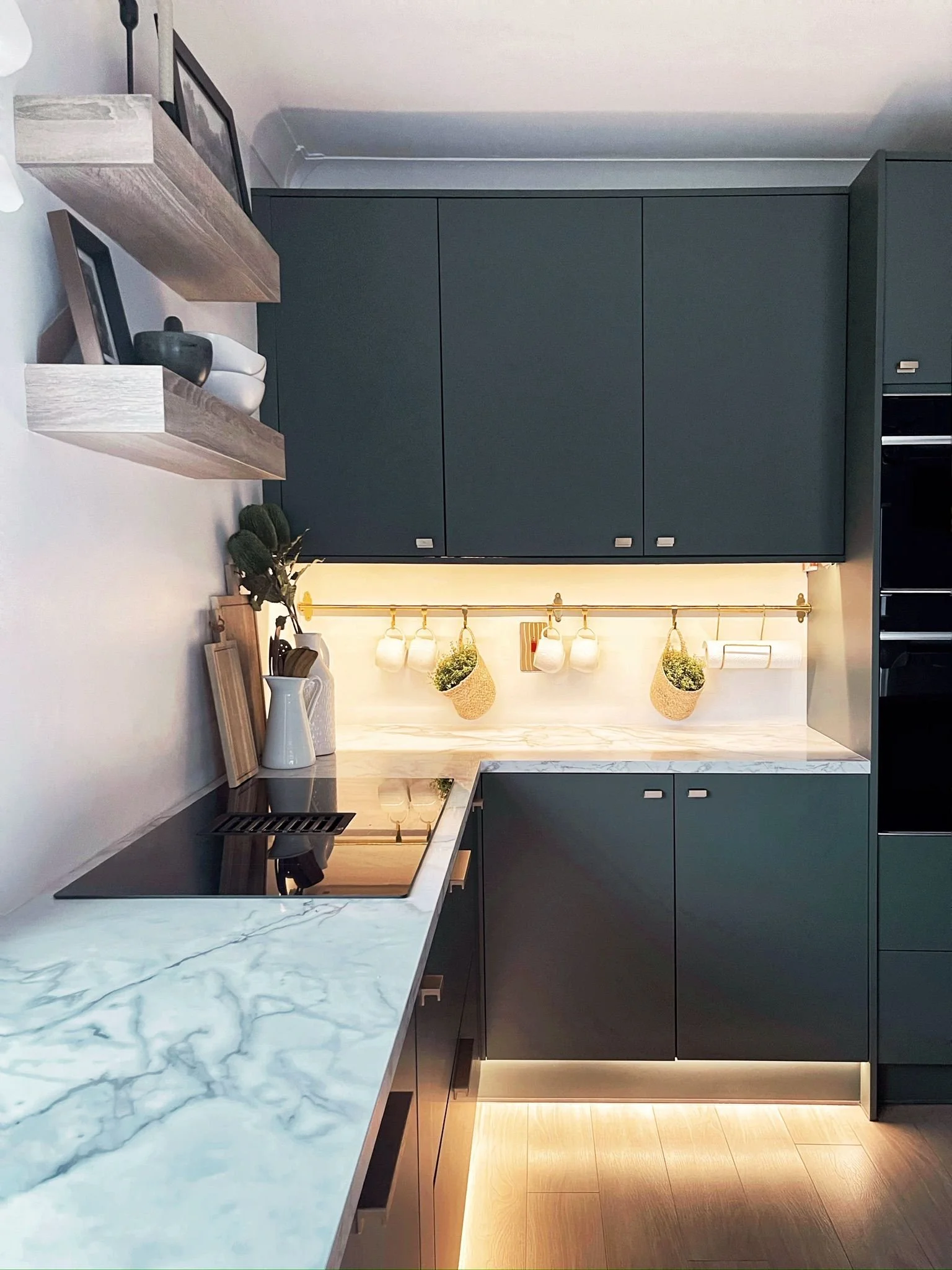 Contemporary kitchen with deep-toned cabinetry, marble-effect worktops, and warm under-cabinet lighting.
