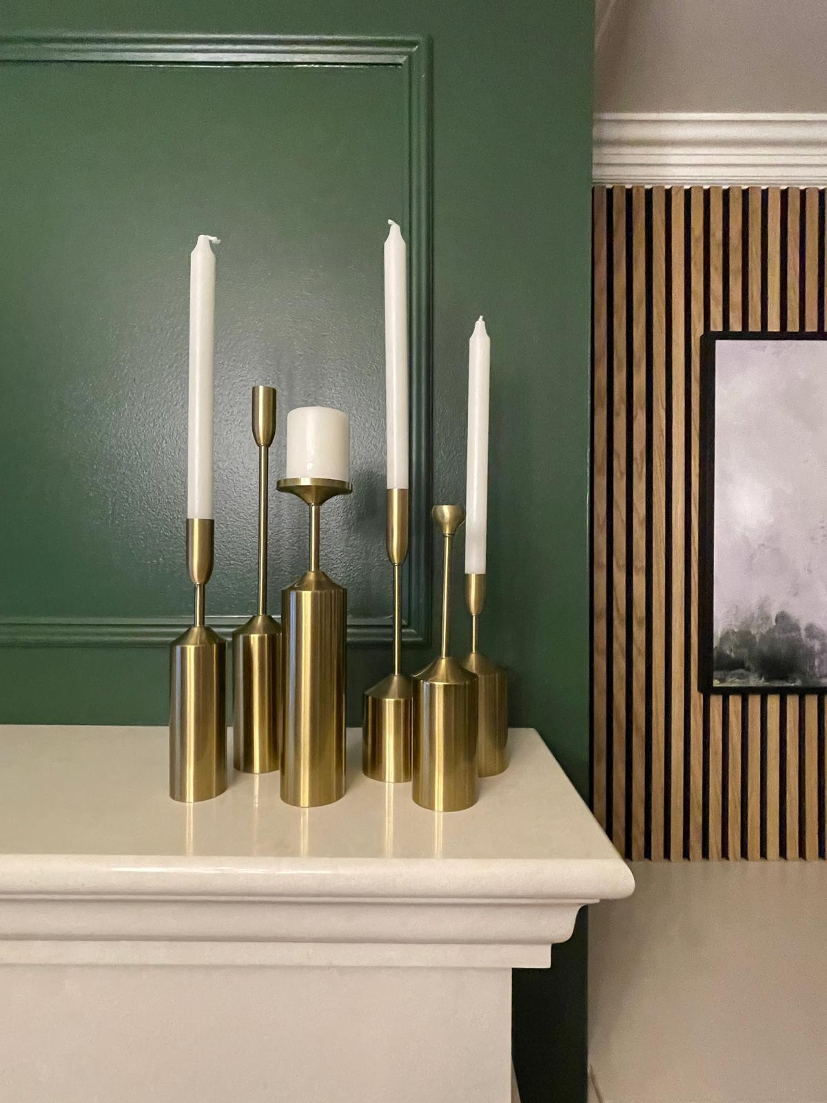 Mantel styling detail with brass candlesticks, deep wall colour, and softly layered decorative finishes.