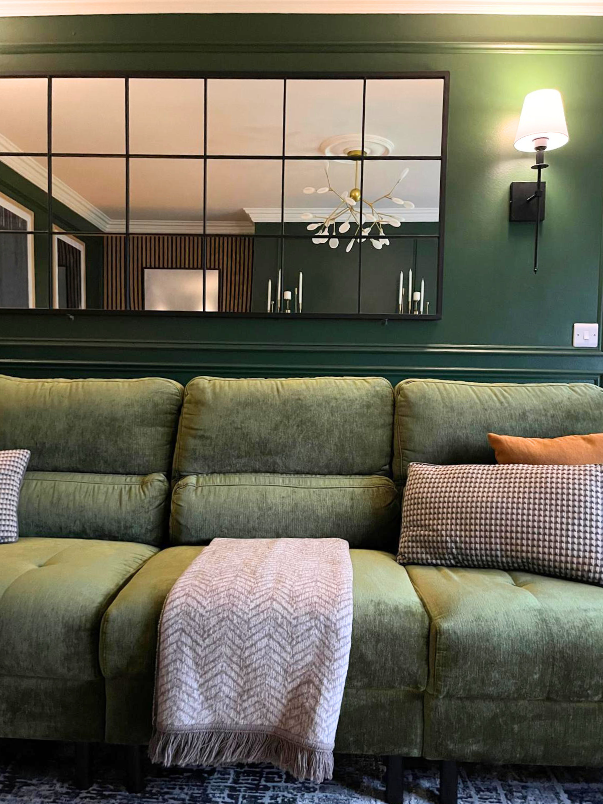 Sectional sofa detail with layered cushions, rich wall colour, and reflective wall panelling for added depth.