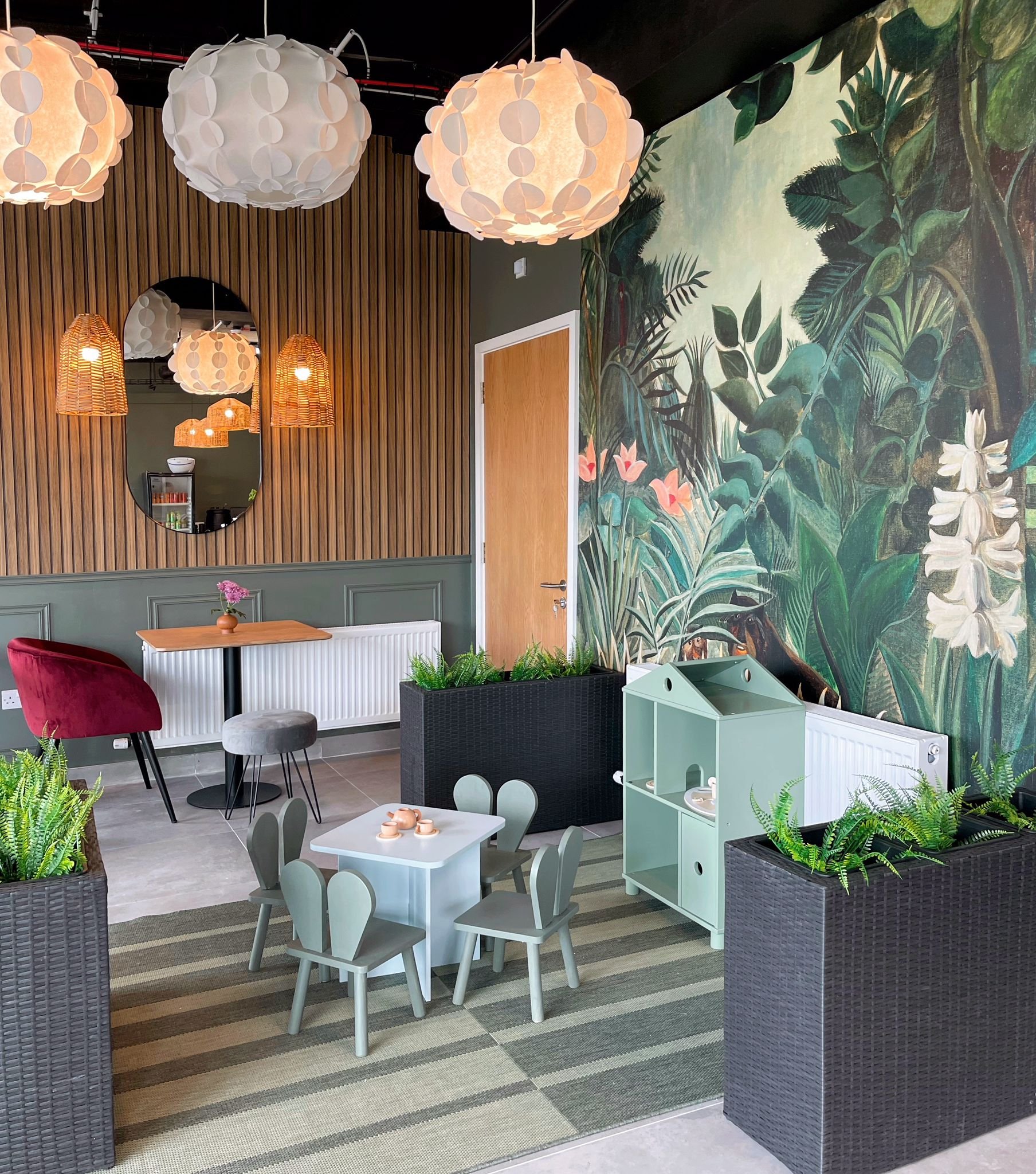 Children’s seating corner with tropical mural wallpaper, timber slat wall, layered pendant lighting, and soft pastel furniture.