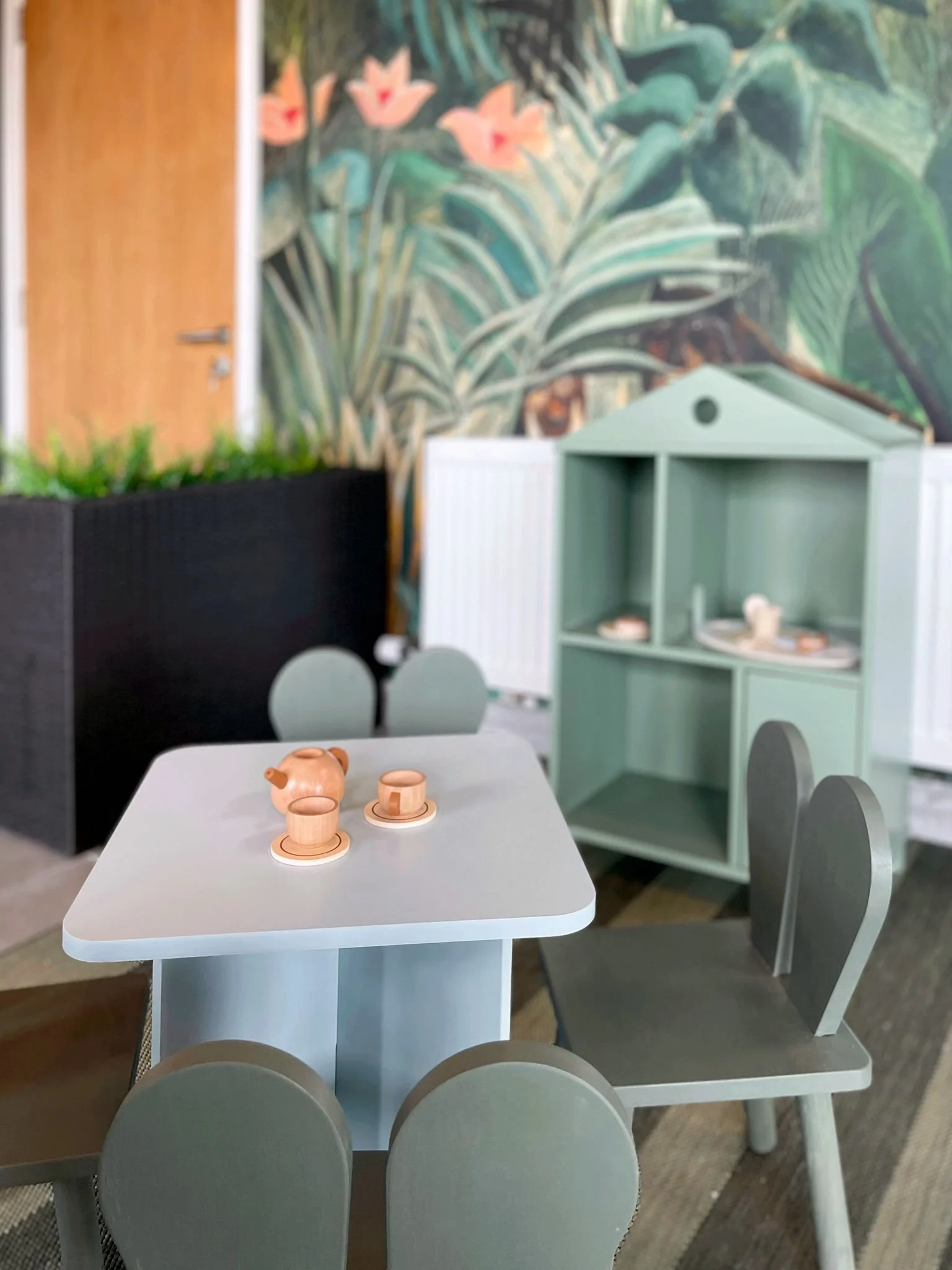 Children’s play corner with pastel furniture, a miniature playhouse shelf, and soft family-friendly styling.