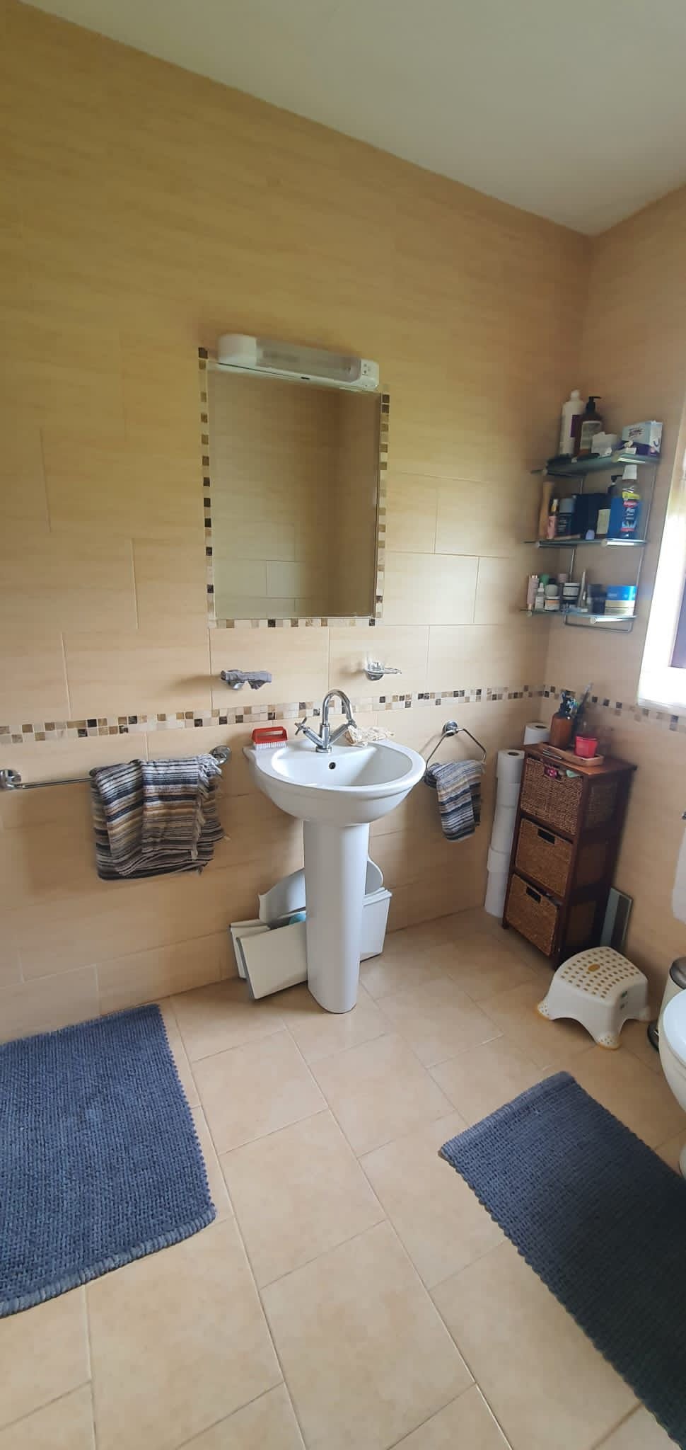 Family bathroom with a pedestal sink, warm neutral finishes, and a simple, functional layout. Before view.