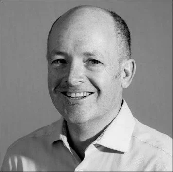 Black and white portrait of a smiling man with short hair, wearing a collared shirt.