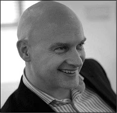 Black and white photo of a man smiling, wearing a collared shirt and blazer.