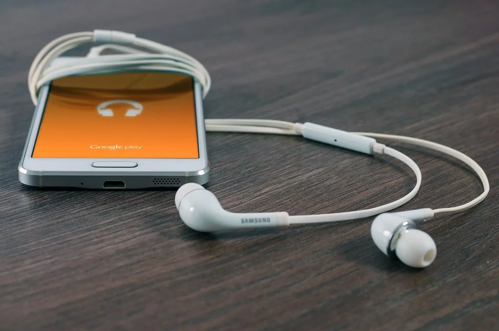 Smartphone with white earbuds resting beside it on a wooden table
