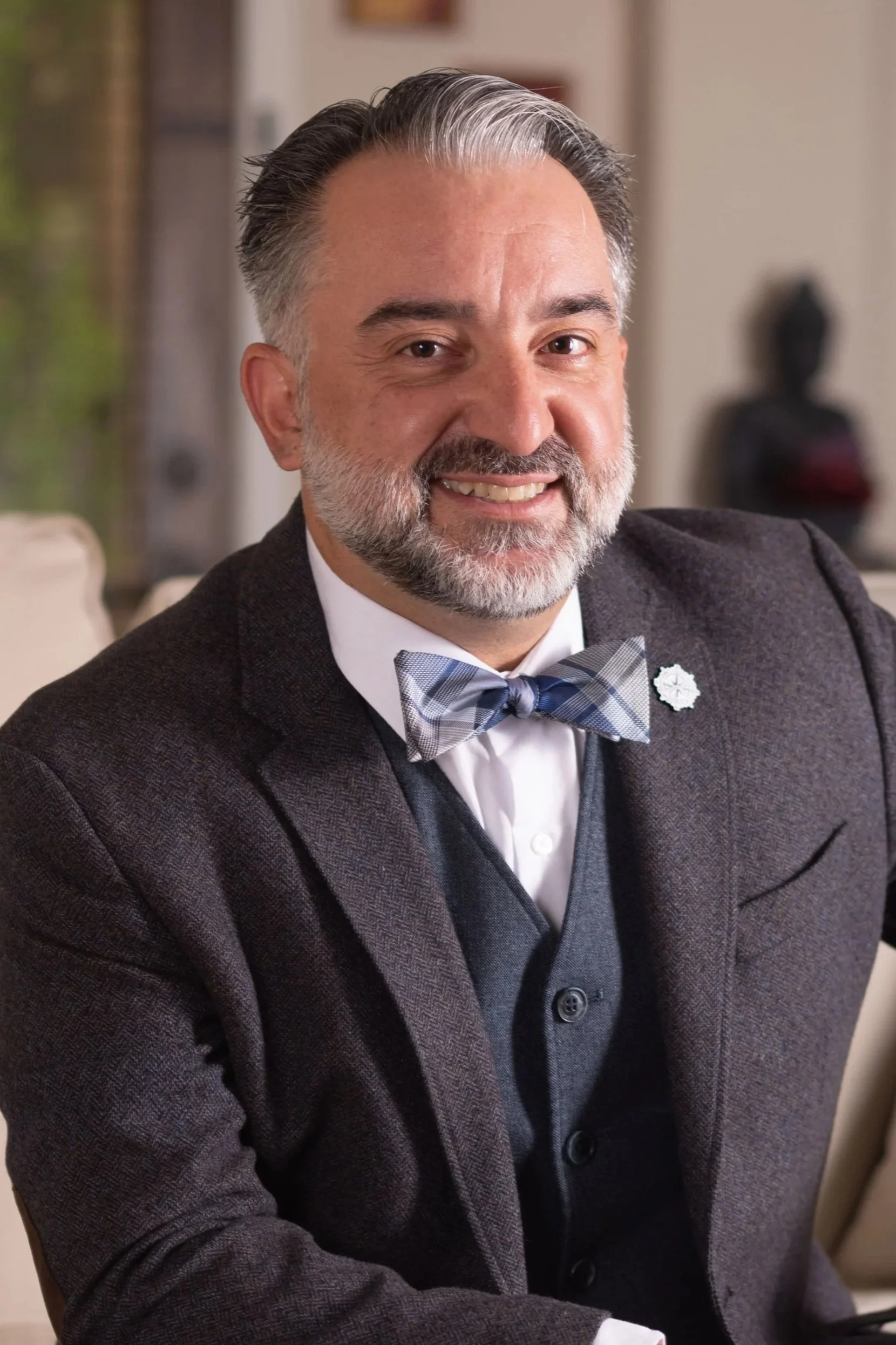 Man wearing glasses and a bow tie standing outdoors in front of a building with glass windows.