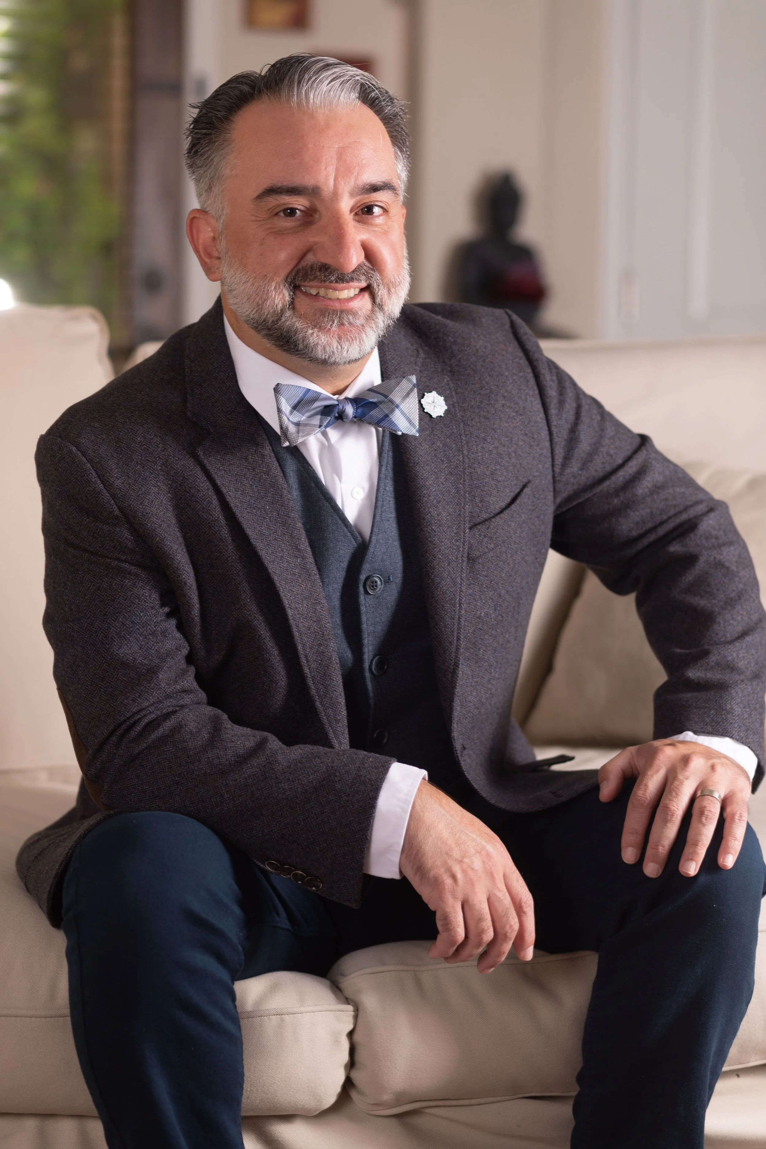 Smiling man in a suit with bowtie sitting on a couch