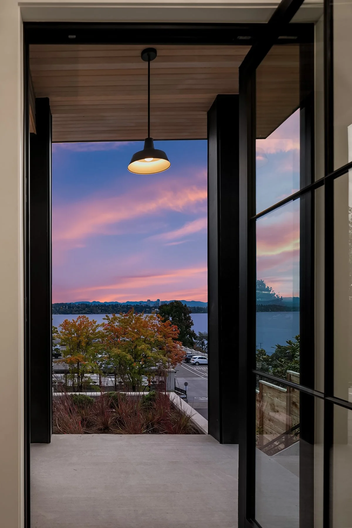 View of a sunset sky with pink and purple clouds, seen through an open balcony door with black framing and a ceiling light inside.