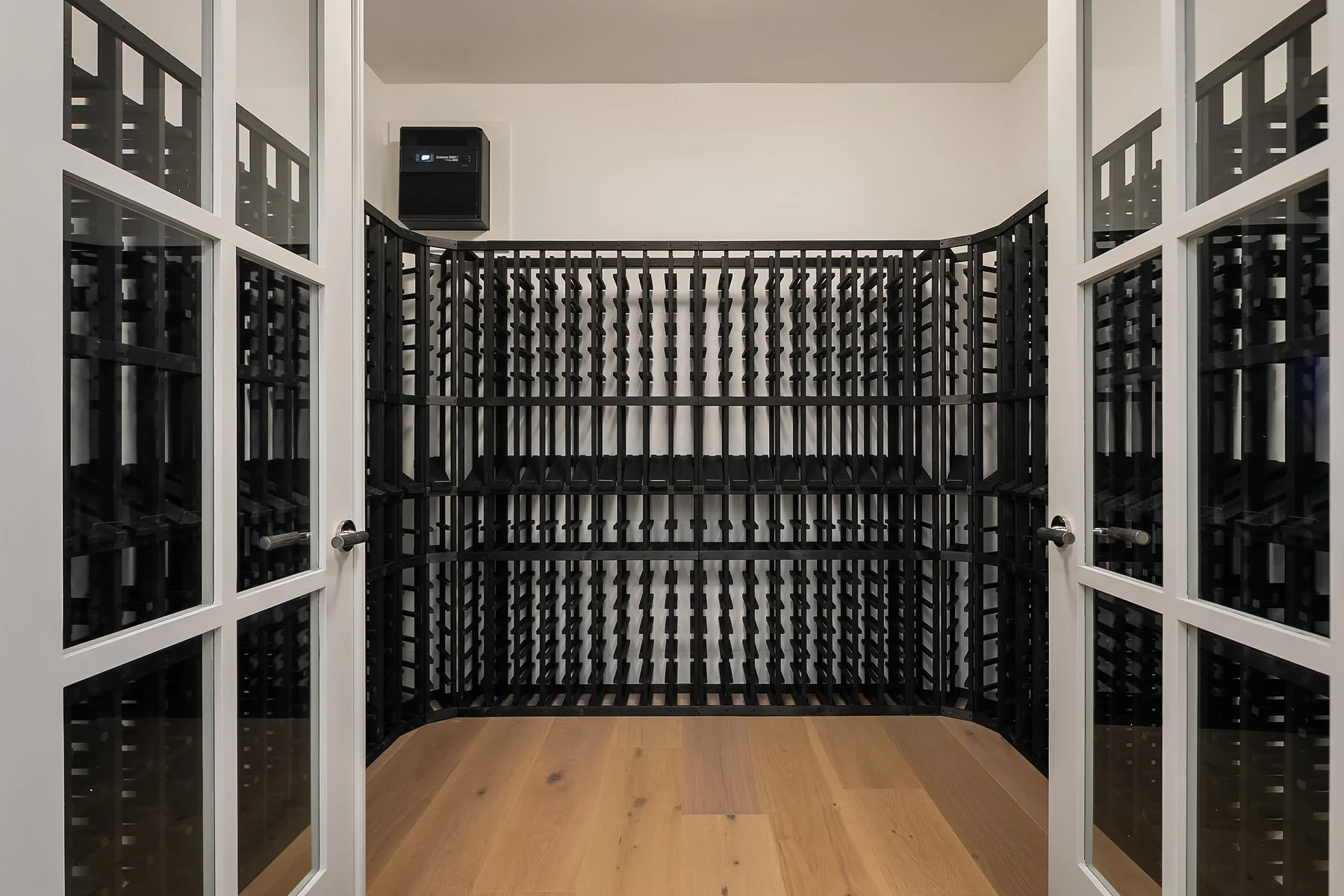 Wine cellar with black wine racks, glass-paneled doors, and a small black wine fridge on the wall.