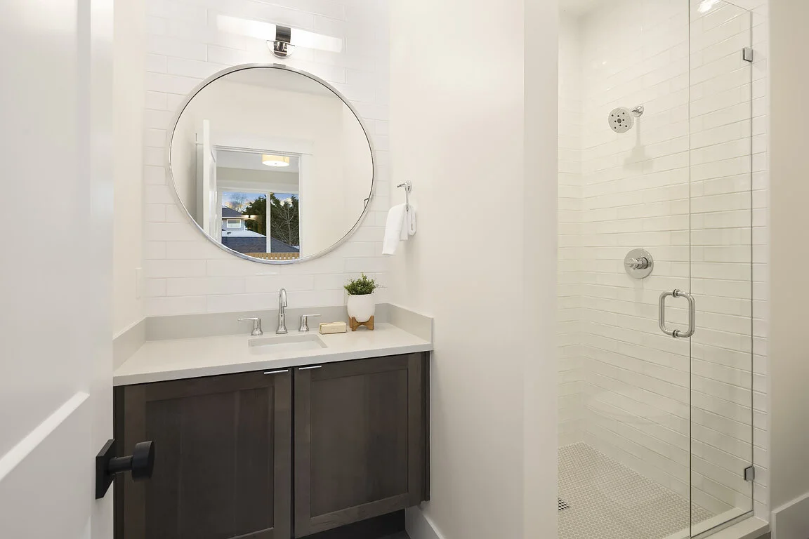 Modern bathroom with a vanity, round mirror, and a glass-enclosed shower.