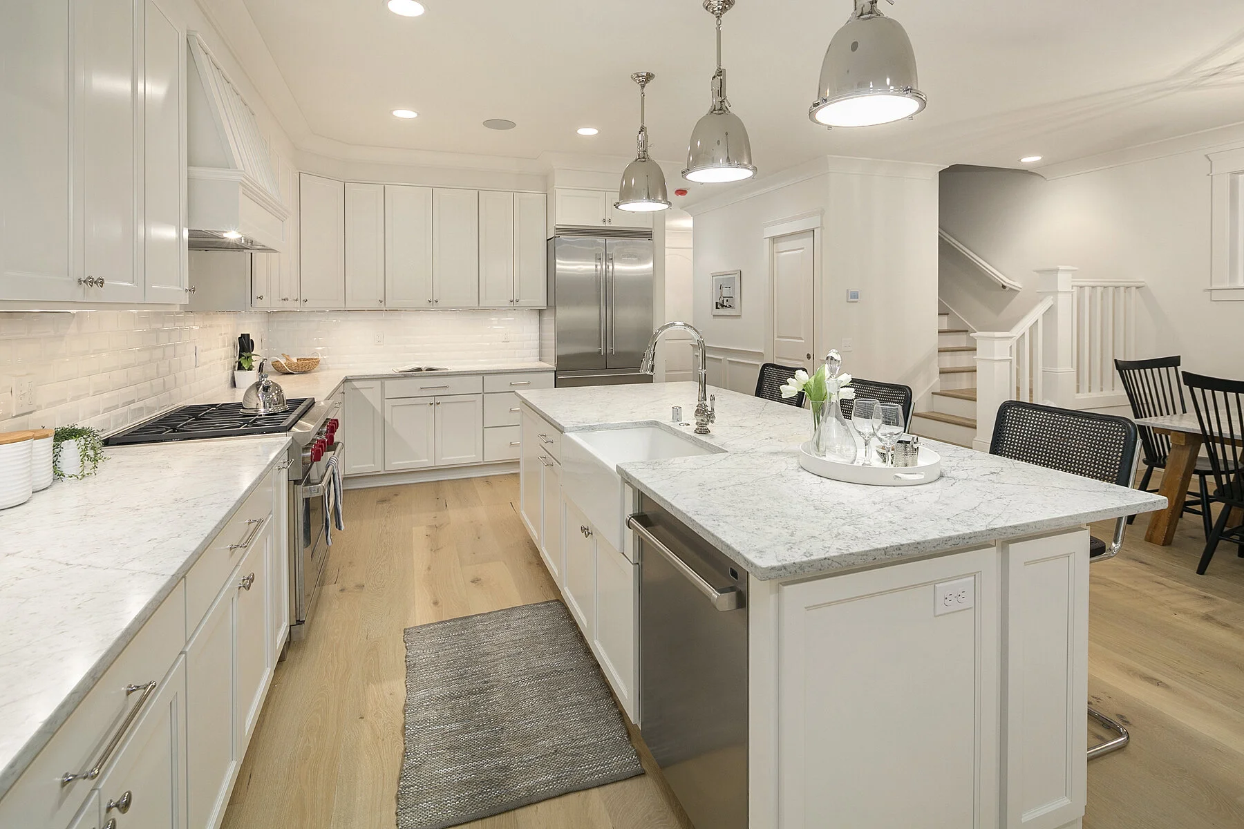 Modern kitchen with white cabinetry, stainless steel appliances, marble countertops, pendant lighting, and a wooden floor.
