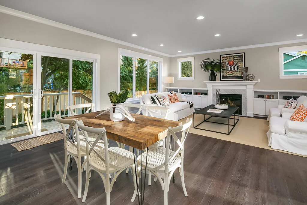 Living room with white sofas, a wooden dining table with white chairs, and large glass sliding doors leading outside.