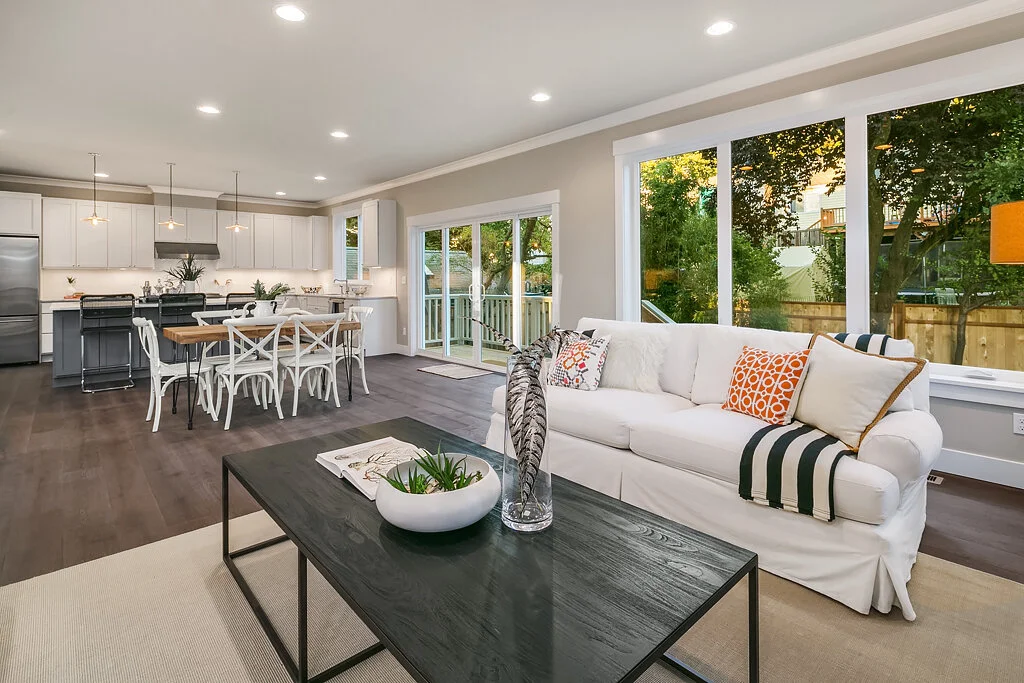 Open-concept living room and kitchen with large windows, white cabinetry, and a dining table, in a modern home.