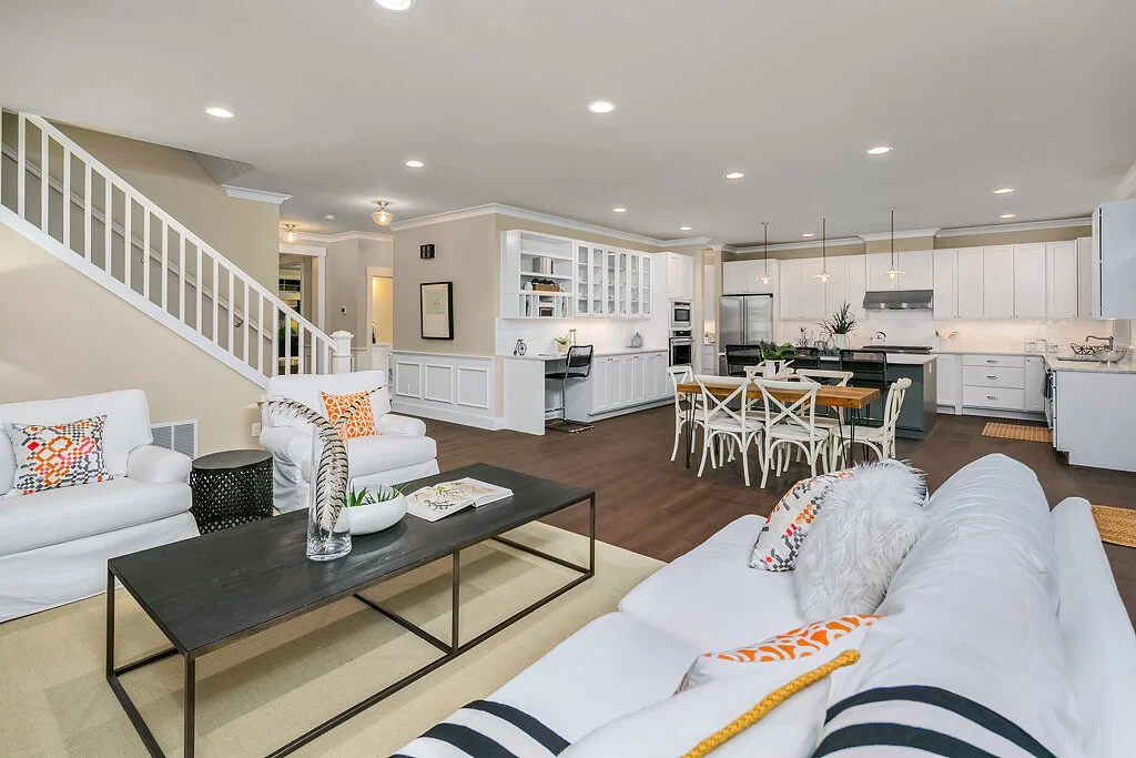 Open-concept living room and kitchen with white furniture, dark hardwood floors, and modern decor.
