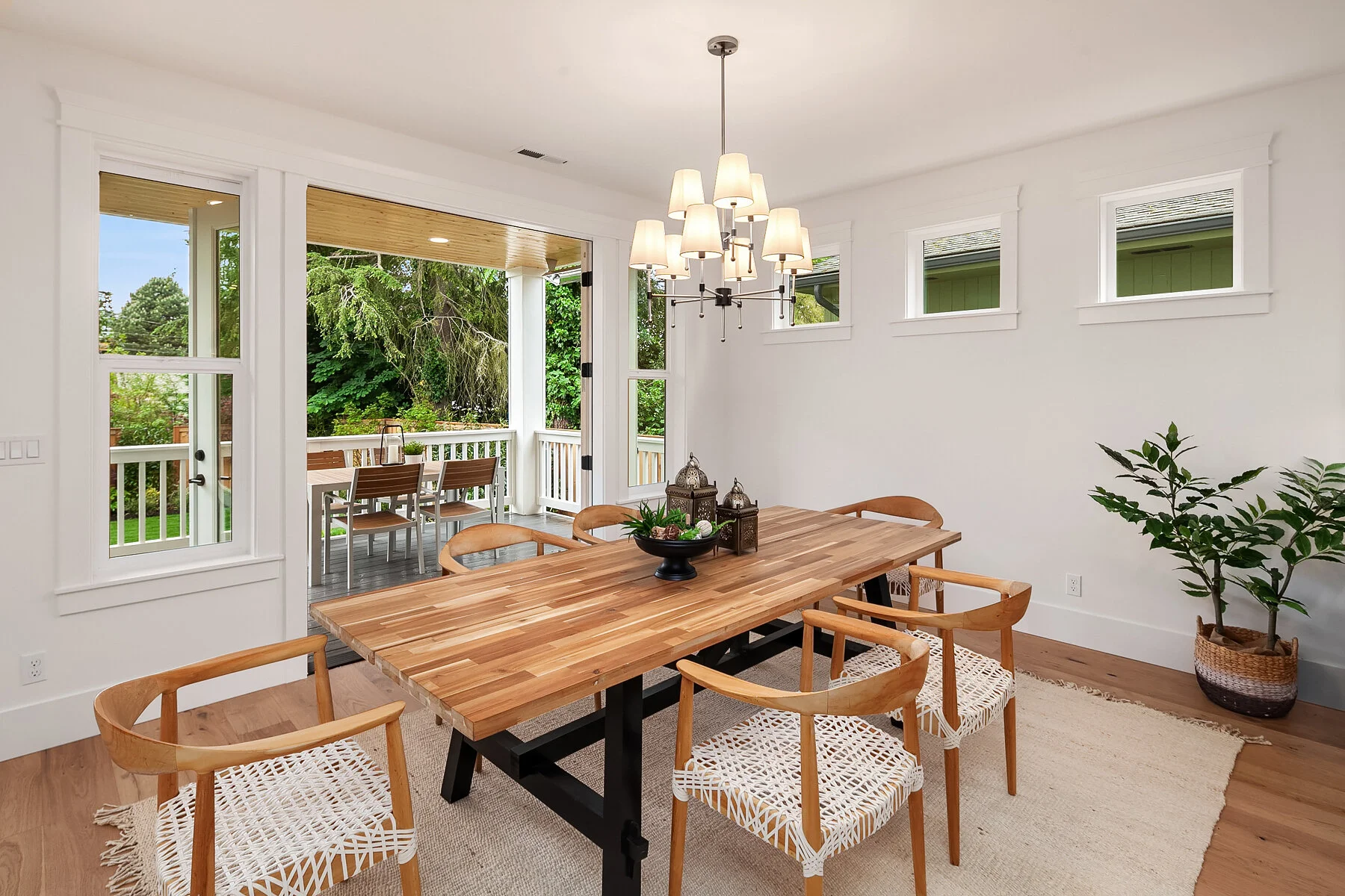 Dining room with a wooden table, wicker chairs, a large pendant chandelier, and an open patio door leading to an outdoor dining area.