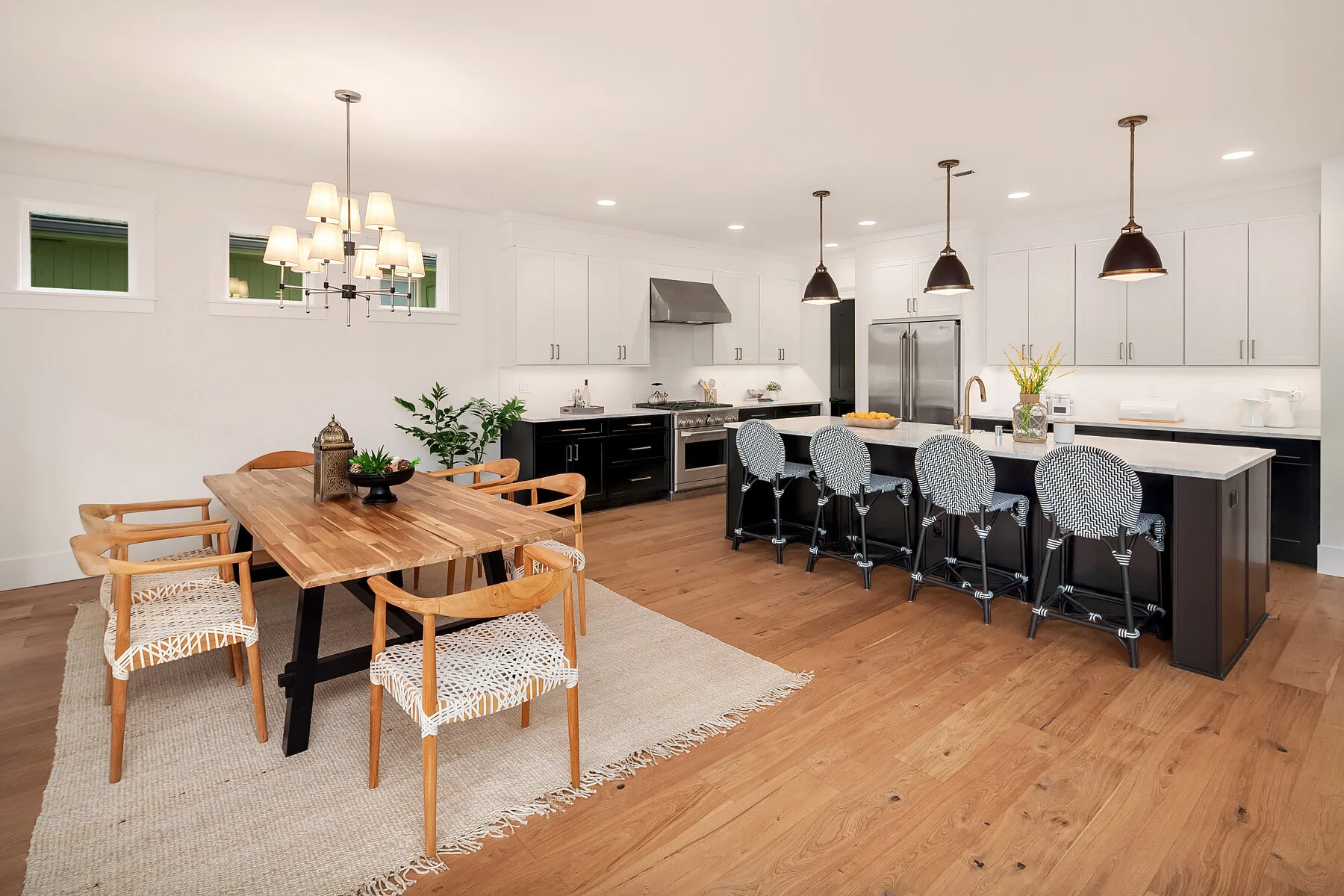 Modern open-plan kitchen and dining area with white cabinets, a black island, wooden dining table with six chairs, and pendant lighting.