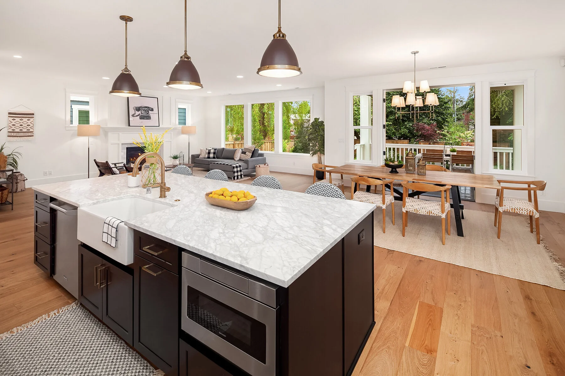 Open-concept kitchen and living room with white walls and large windows, featuring a marble kitchen island, dining table with chairs, and a gray sofa in the living area.