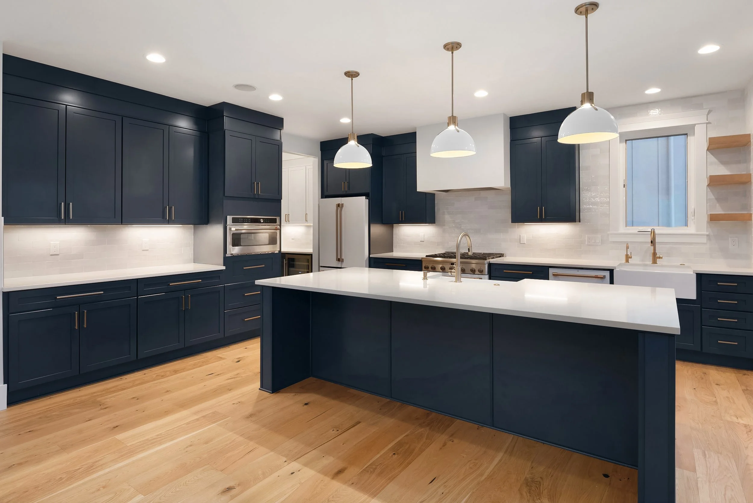 Modern kitchen with navy blue cabinets, white countertops, a central island, hardwood floors, and pendant lighting.