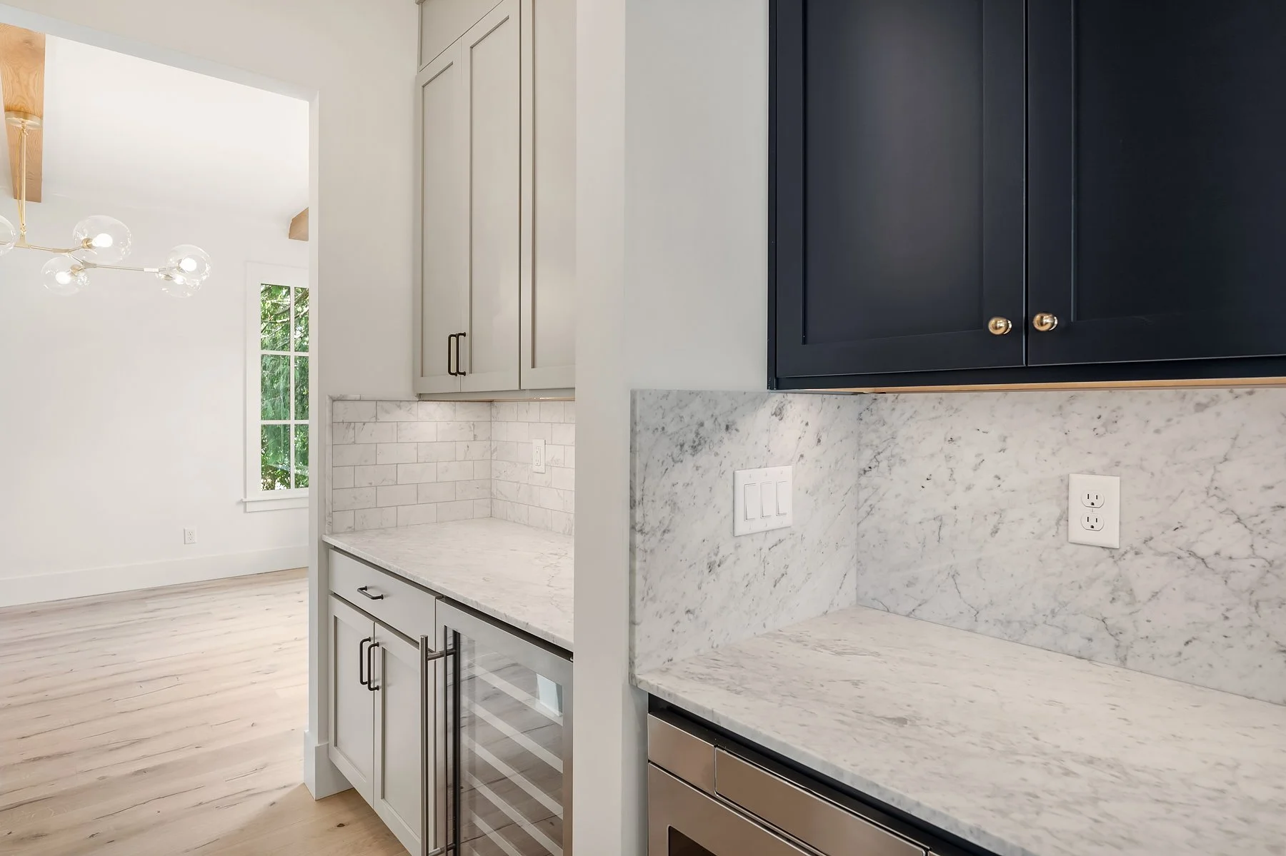 Kitchen with white and navy cabinets, marble countertops, and a marble backsplash. A small wine fridge is built into the lower cabinet, and there are outlets on the backsplash.