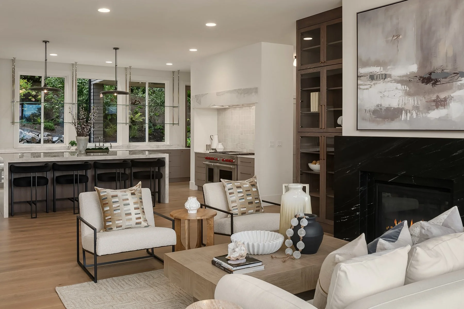 Open-concept living room and kitchen with large windows, wood flooring, modern fireplace, and minimalist decor.