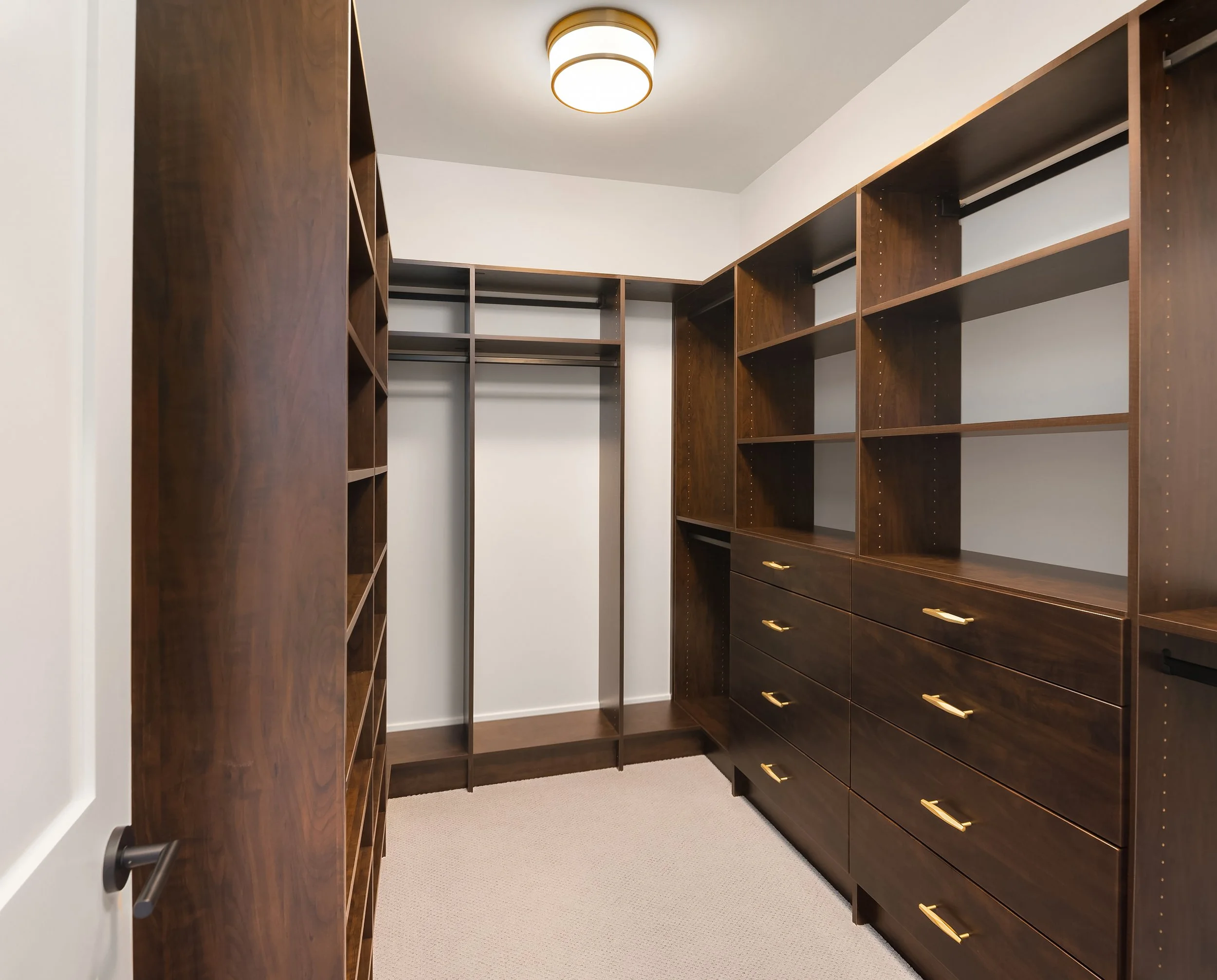 Empty walk-in closet with dark wood shelving and drawers, beige carpet, and white walls.
