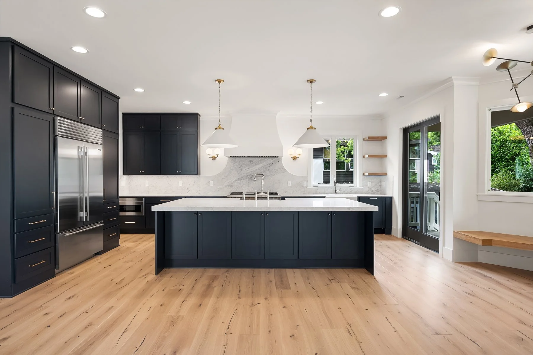 Modern kitchen with black cabinets, white marble countertops, a large kitchen island, stainless steel appliances, and hardwood floors.