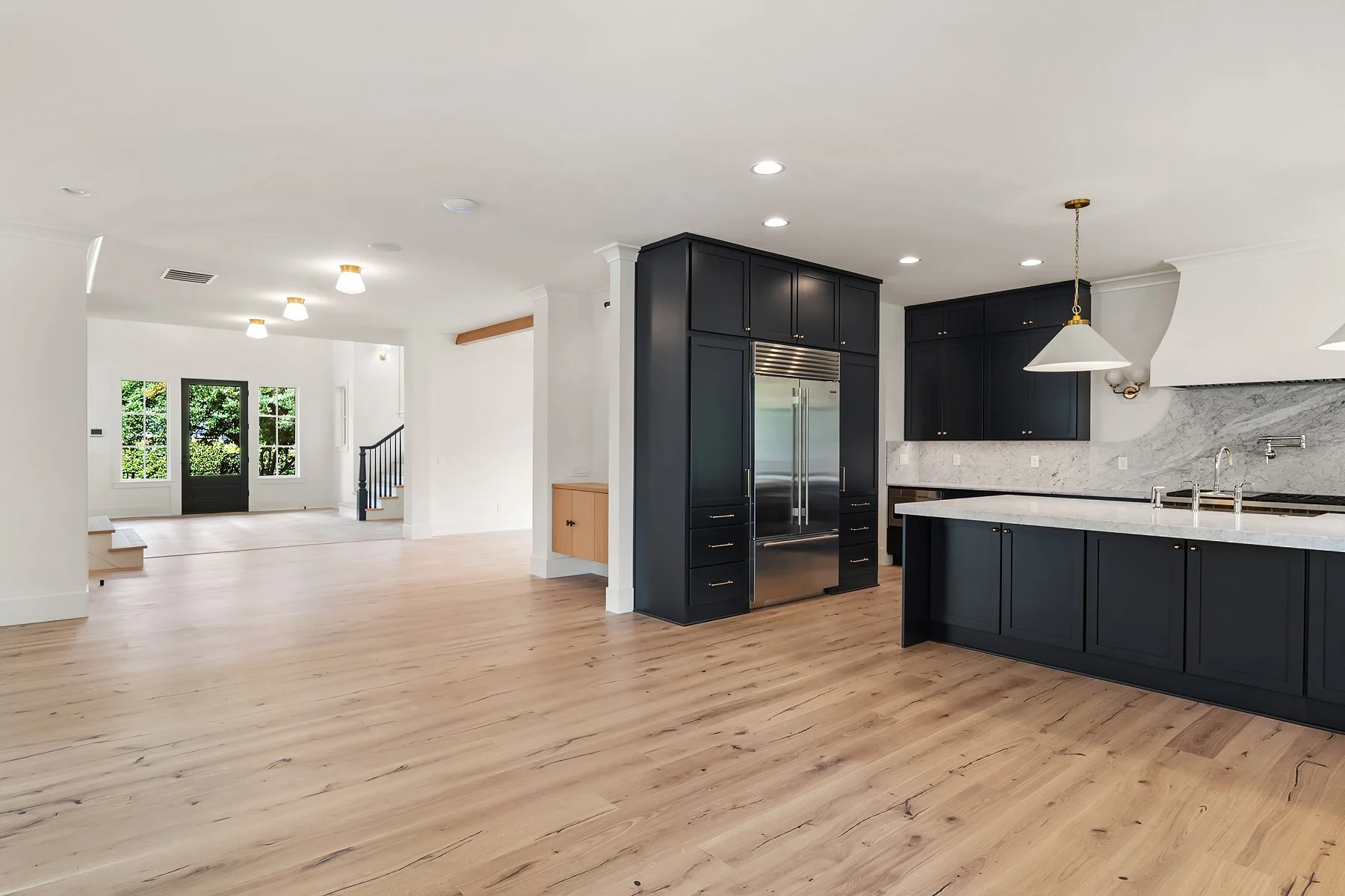 Spacious kitchen with black cabinets, white marble countertops, stainless steel appliances, and light-colored hardwood floors.