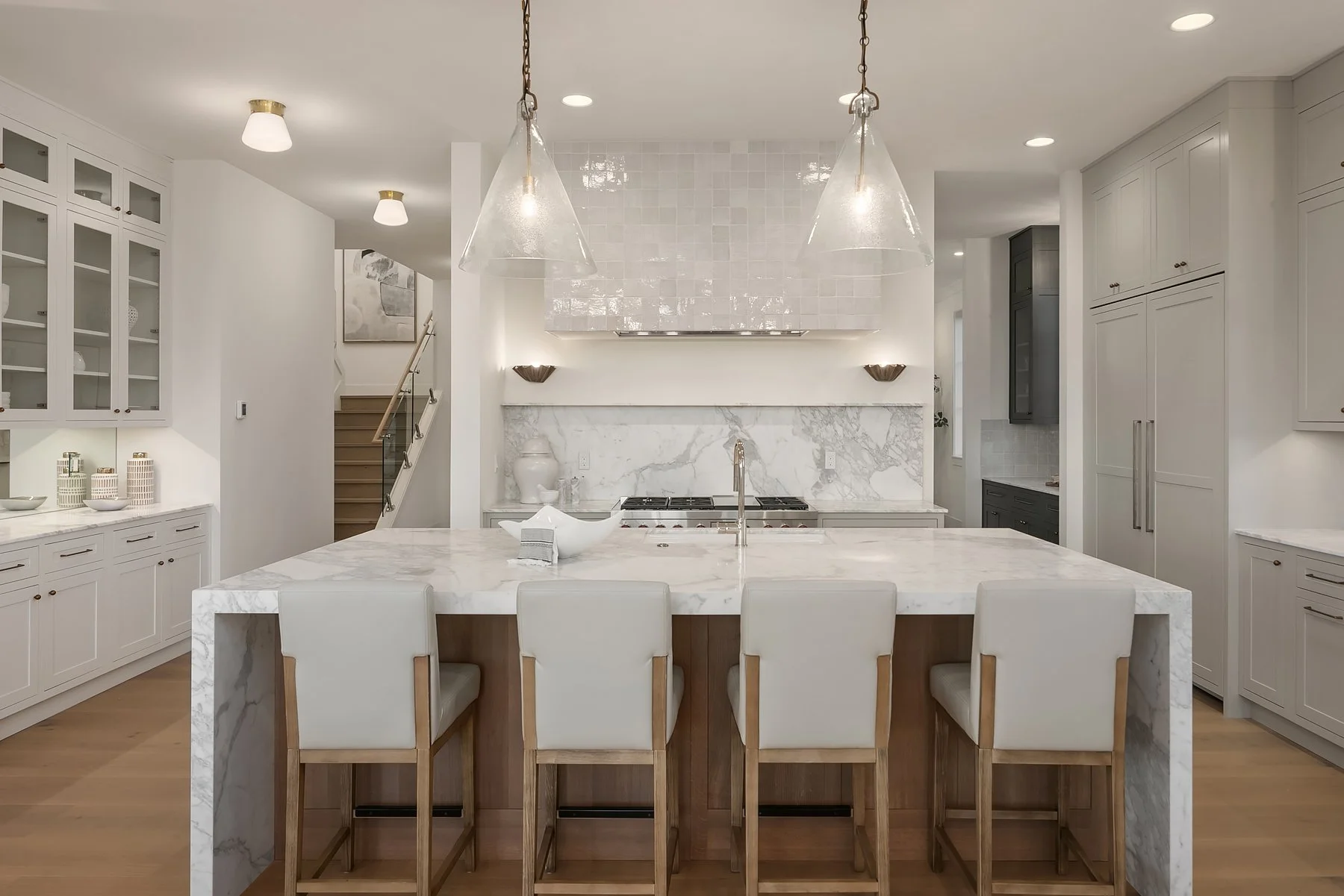 Modern kitchen with white marble island, pendant lighting, white cabinetry, and a stove with a marble backsplash.