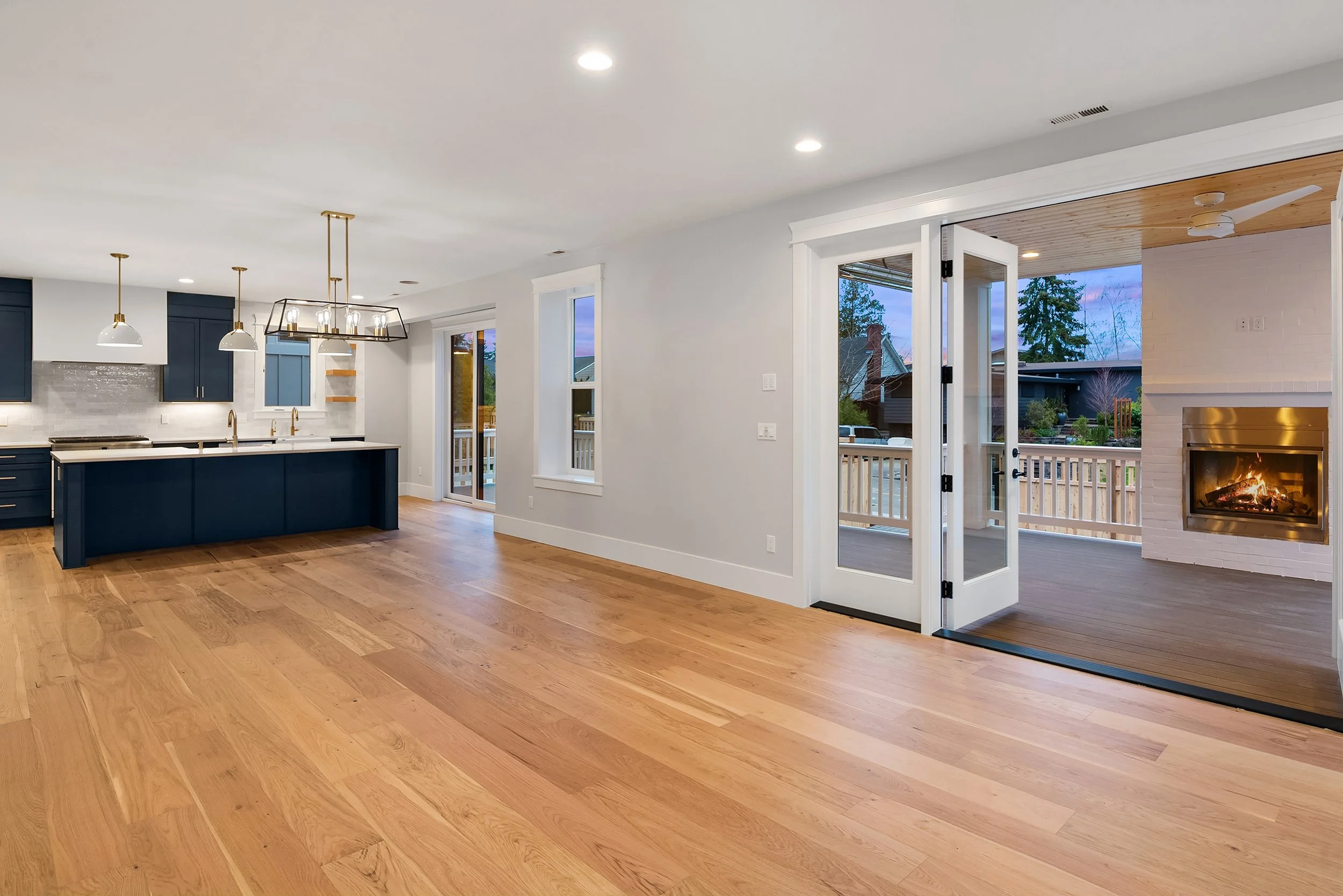 Open living space with hardwood floors, a kitchen with navy blue cabinets, pendant lighting, and a backyard with a deck and a fireplace