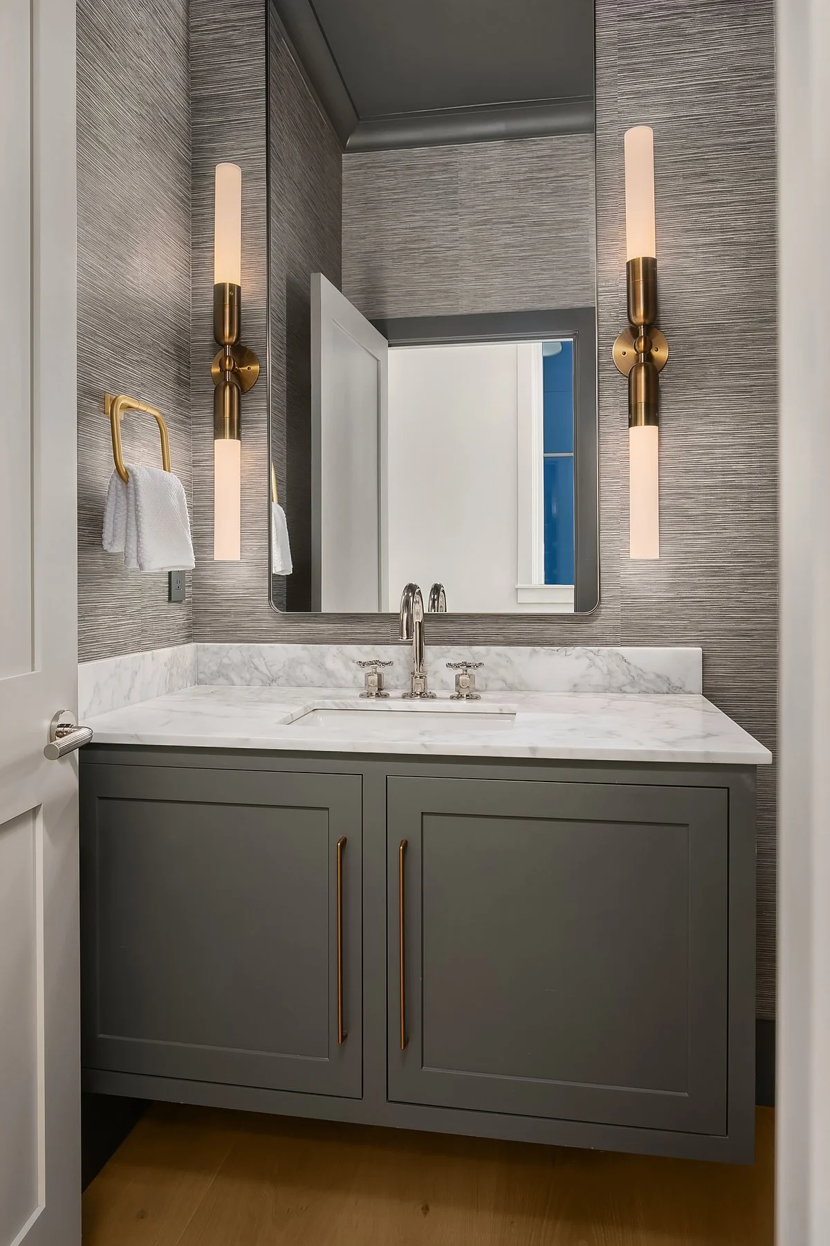 Modern bathroom vanity with gray cabinet, white marble countertop, and silver faucet, flanked by two tall vertical wall sconces with brass accents, and a large rectangular mirror above.