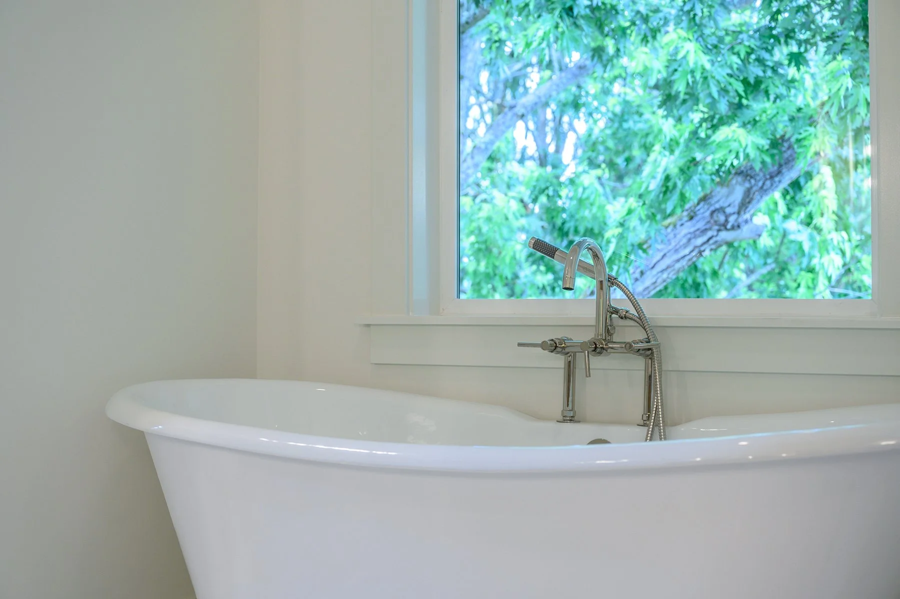 White bathtub with vintage faucet near window with green trees outside.