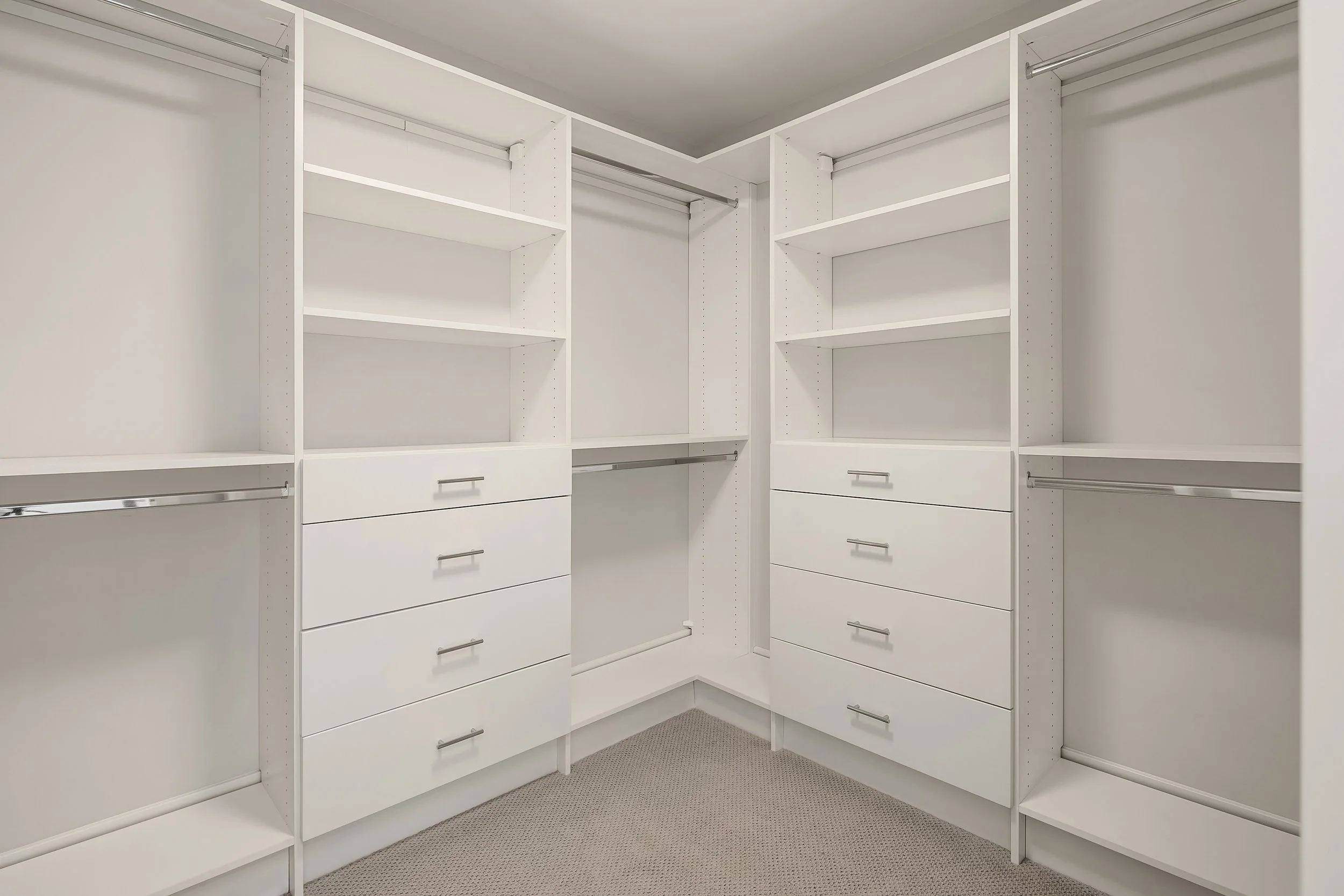 Empty white walk-in closet with built-in shelves, drawers, and hanging rods.
