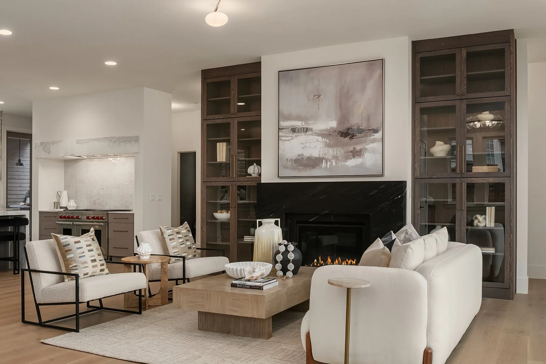 Modern living room with white sofa, armchairs, a wooden coffee table, fireplace, and built-in wooden shelves