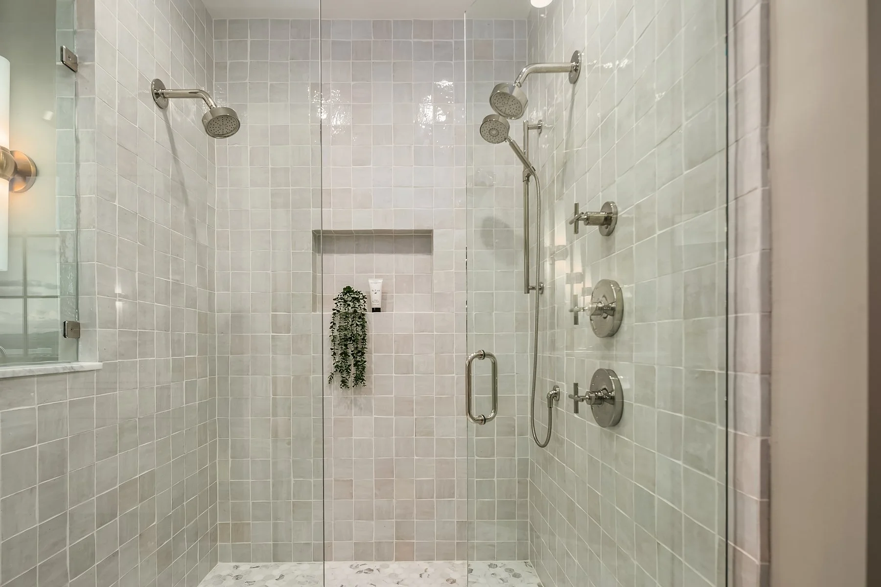 Modern walk-in shower with glass door, multiple showerheads, and beige tiled walls.