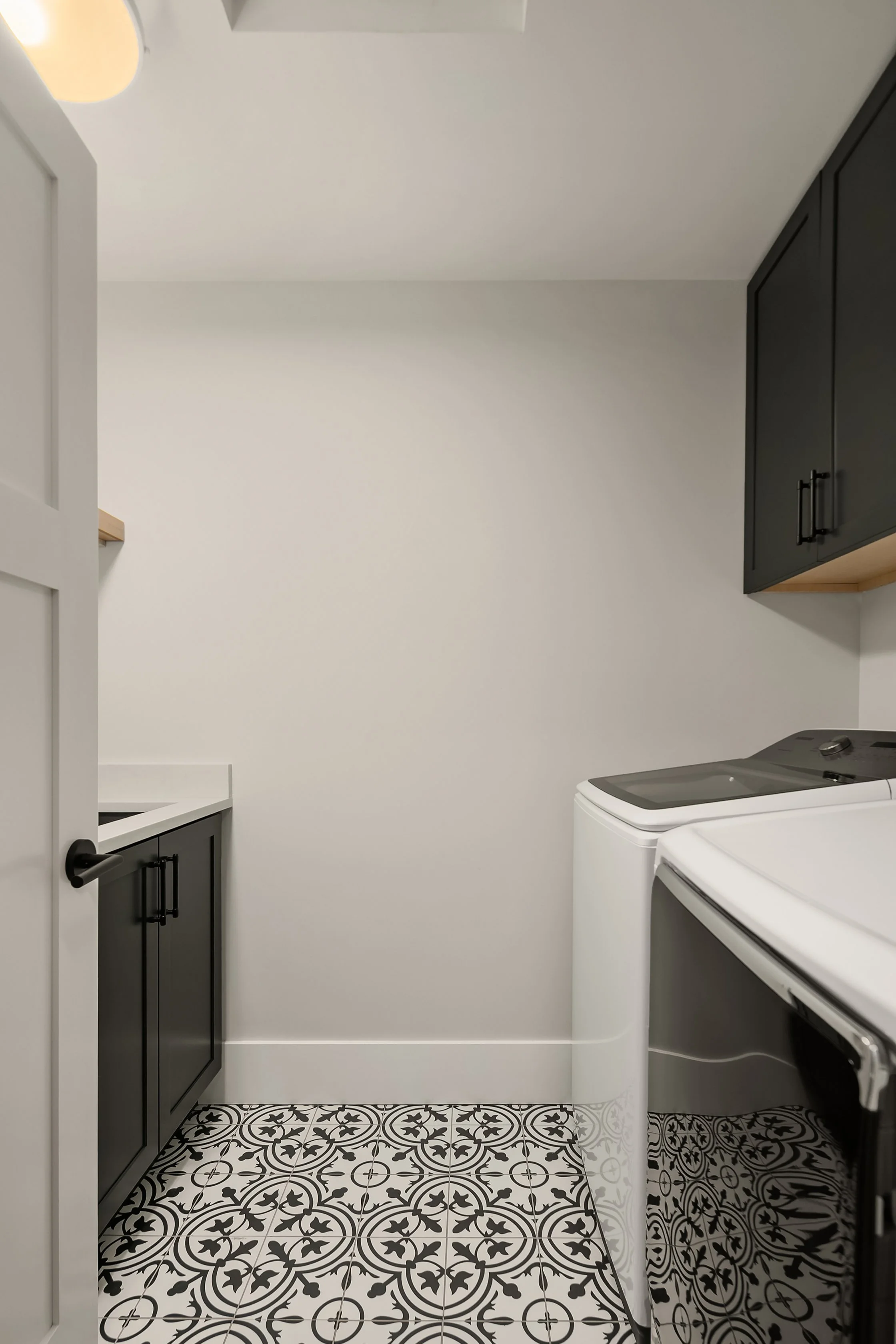 Laundry room with black cabinets, white walls, a white washing machine, and black and white patterned floor tiles.