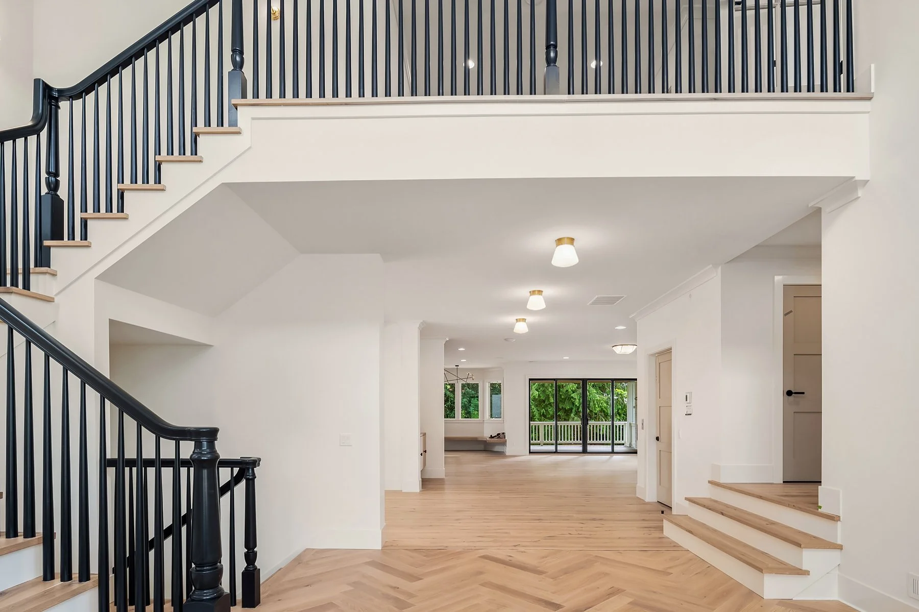Bright, spacious living area with white walls, light wood flooring, and large sliding glass doors leading to an outdoor balcony