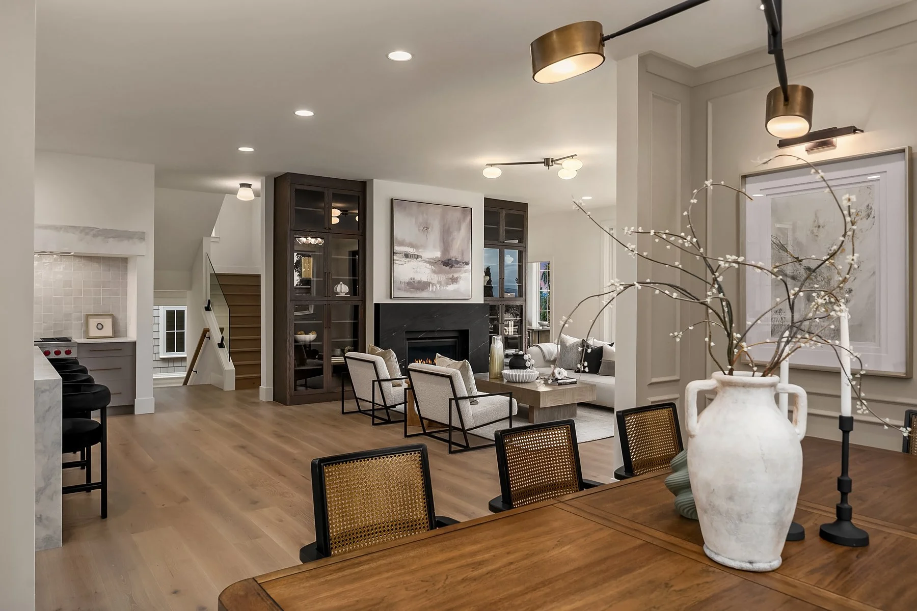 Open-concept living and dining room with wooden floors, modern furniture, a fireplace, built-in shelves, and decorative vases and artwork.