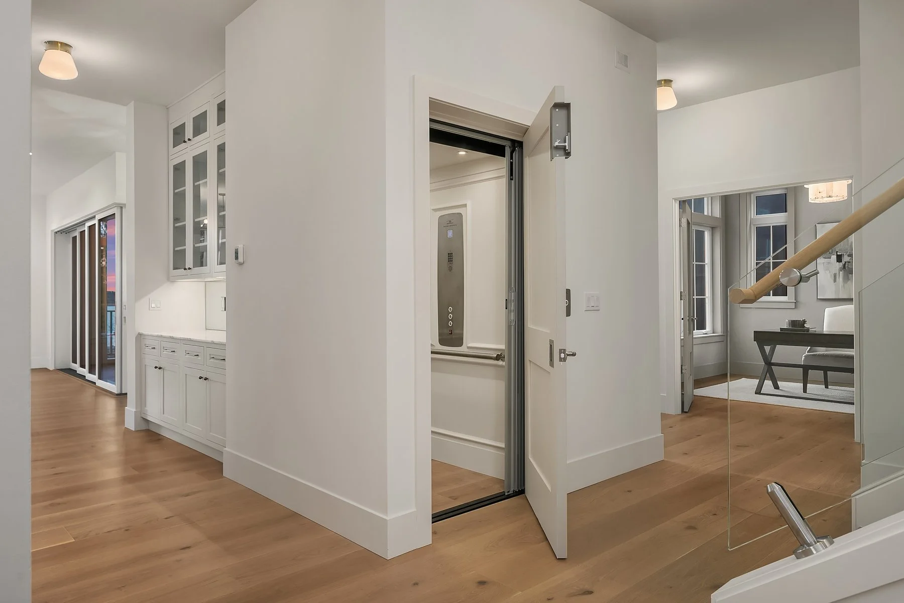 Modern home interior with an elevator, hardwood floors, built-in white cabinetry, and large windows