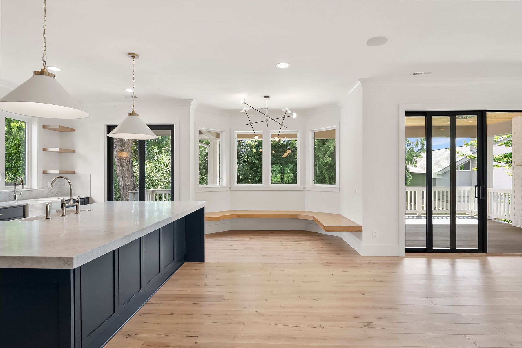 Modern kitchen with white countertops, navy blue cabinets, light wood flooring, large windows, and sliding glass door leading to a balcony.