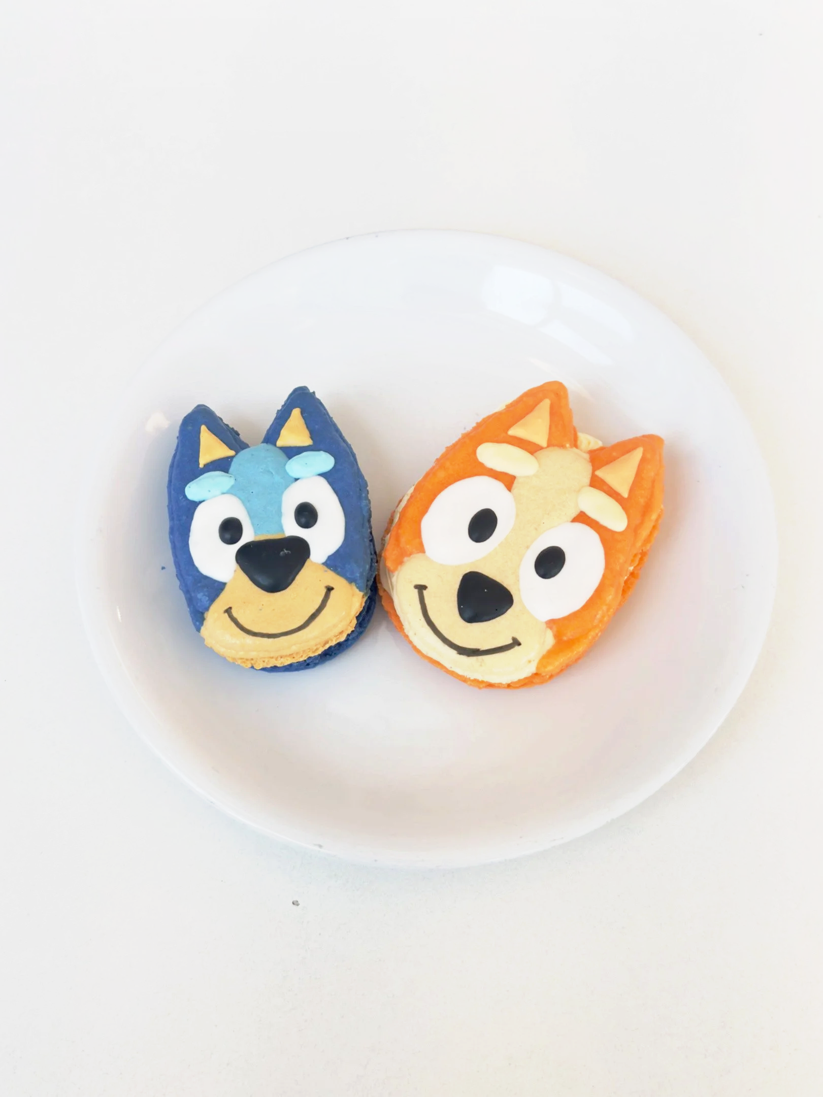 Decorated cookies shaped like cartoon dogs, one blue and one orange, on a white plate — custom dessert catering and events by Decadent Macaron in Gilbert, Arizona
