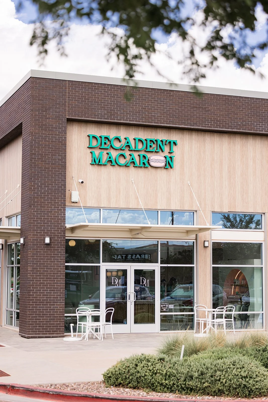 Exterior of Decadent Macaron bakery with glass storefront, white chairs outside, and a sign with teal lettering and a macaron graphic — Decadent Macaron café in Gilbert, Arizona dessert shop and specialty café