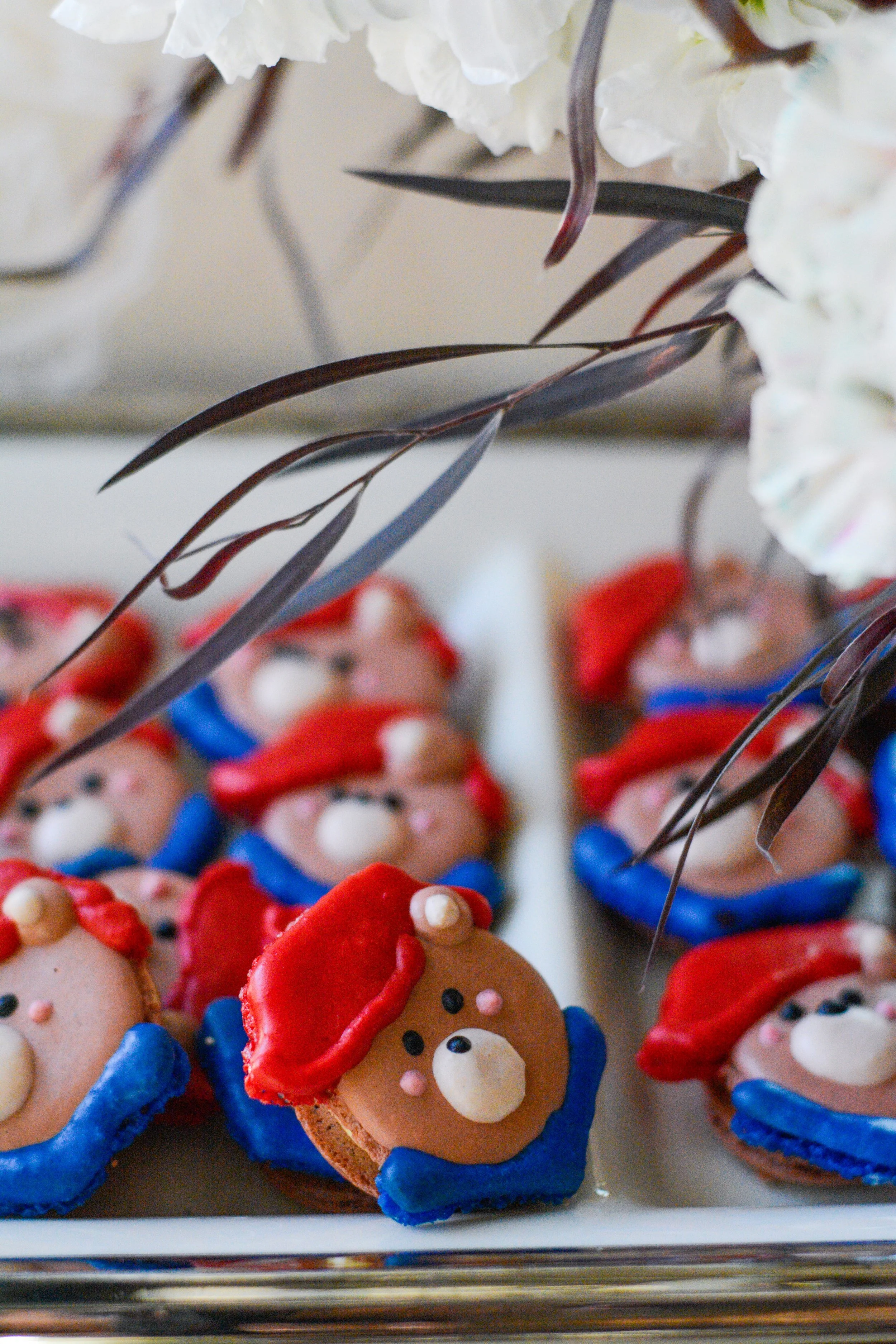 Plate of cookies decorated as bears with red hats and blue collars, featuring facial details like eyes and noses — custom dessert catering and events by Decadent Macaron in Gilbert, Arizona