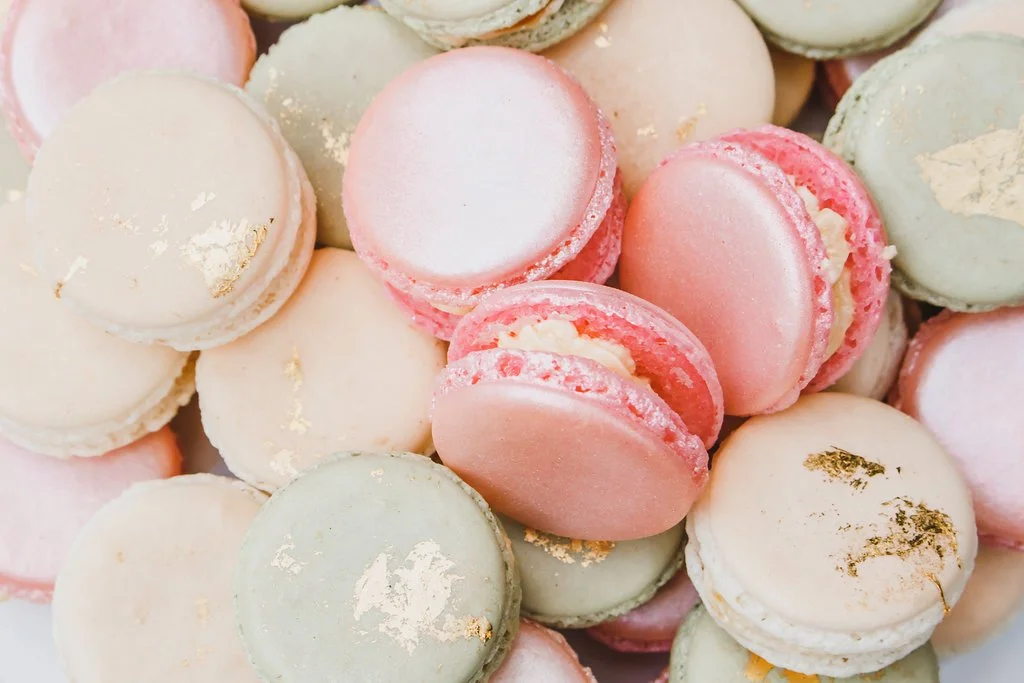 Close-up of colorful macarons in pastel shades of pink, white, and green, some with gold leaf accents — custom dessert catering and events by Decadent Macaron in Gilbert, Arizona